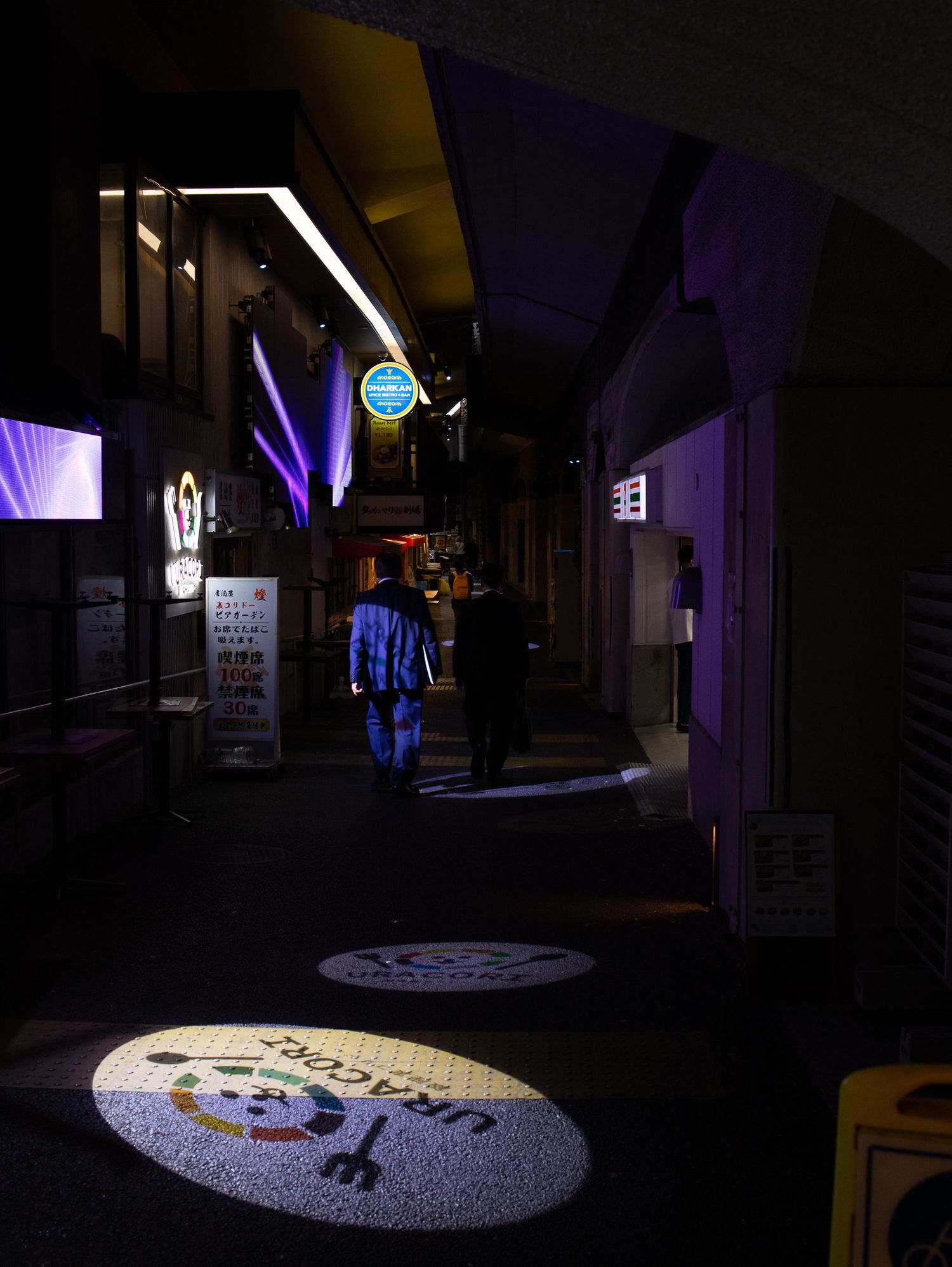 Dark hallway with purple lighting and spotlit circular displays on the floor.