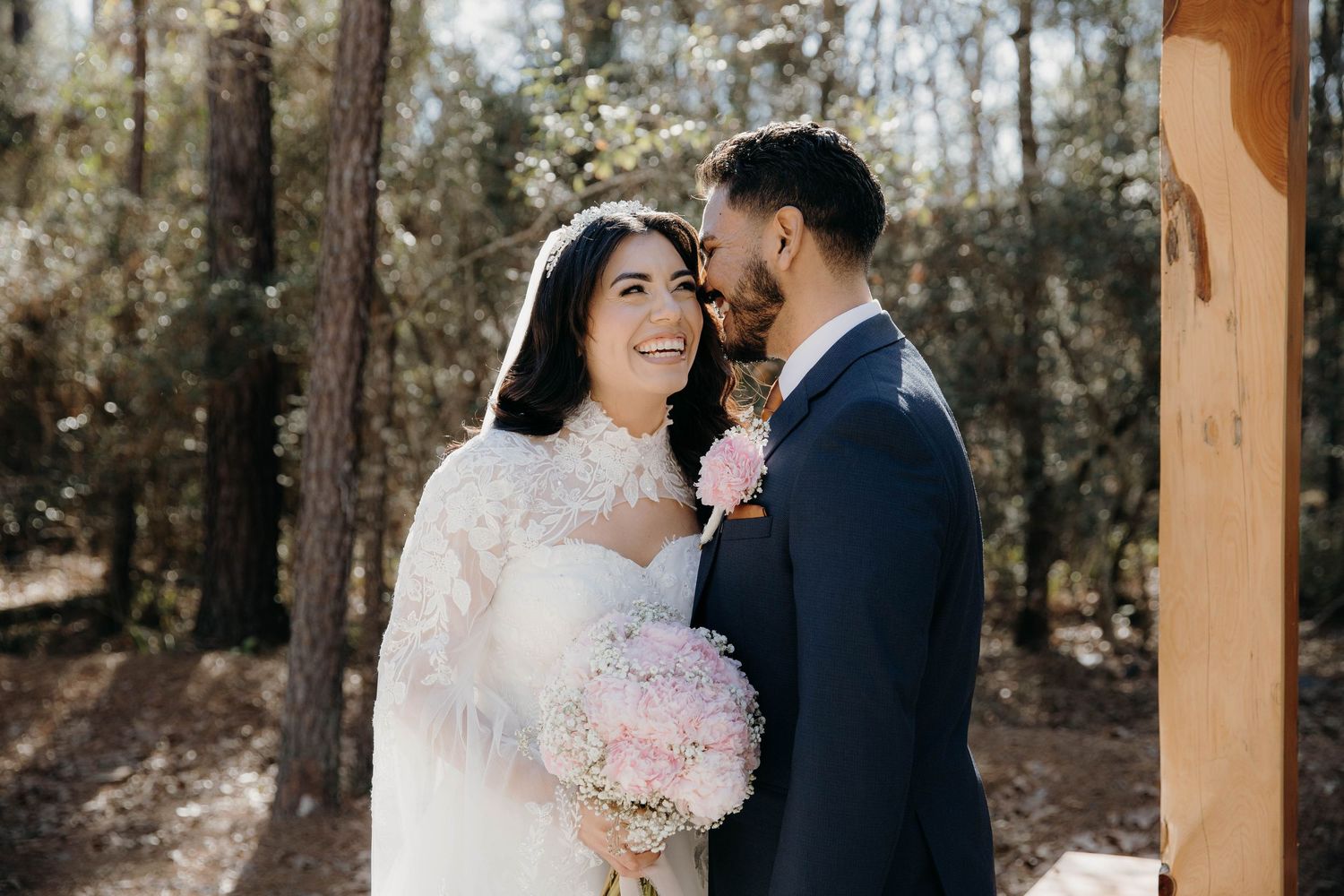 A couple in wedding attire shares intimate moments in a wooded setting with natural light filtering through trees.