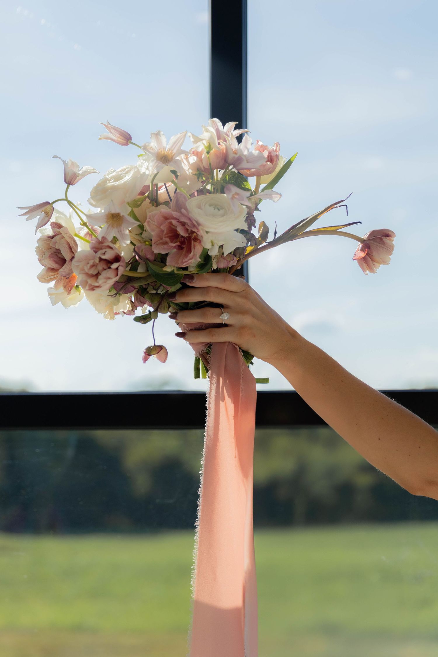 Hands arranging pink and white flowers in a coral vase against blue sky.