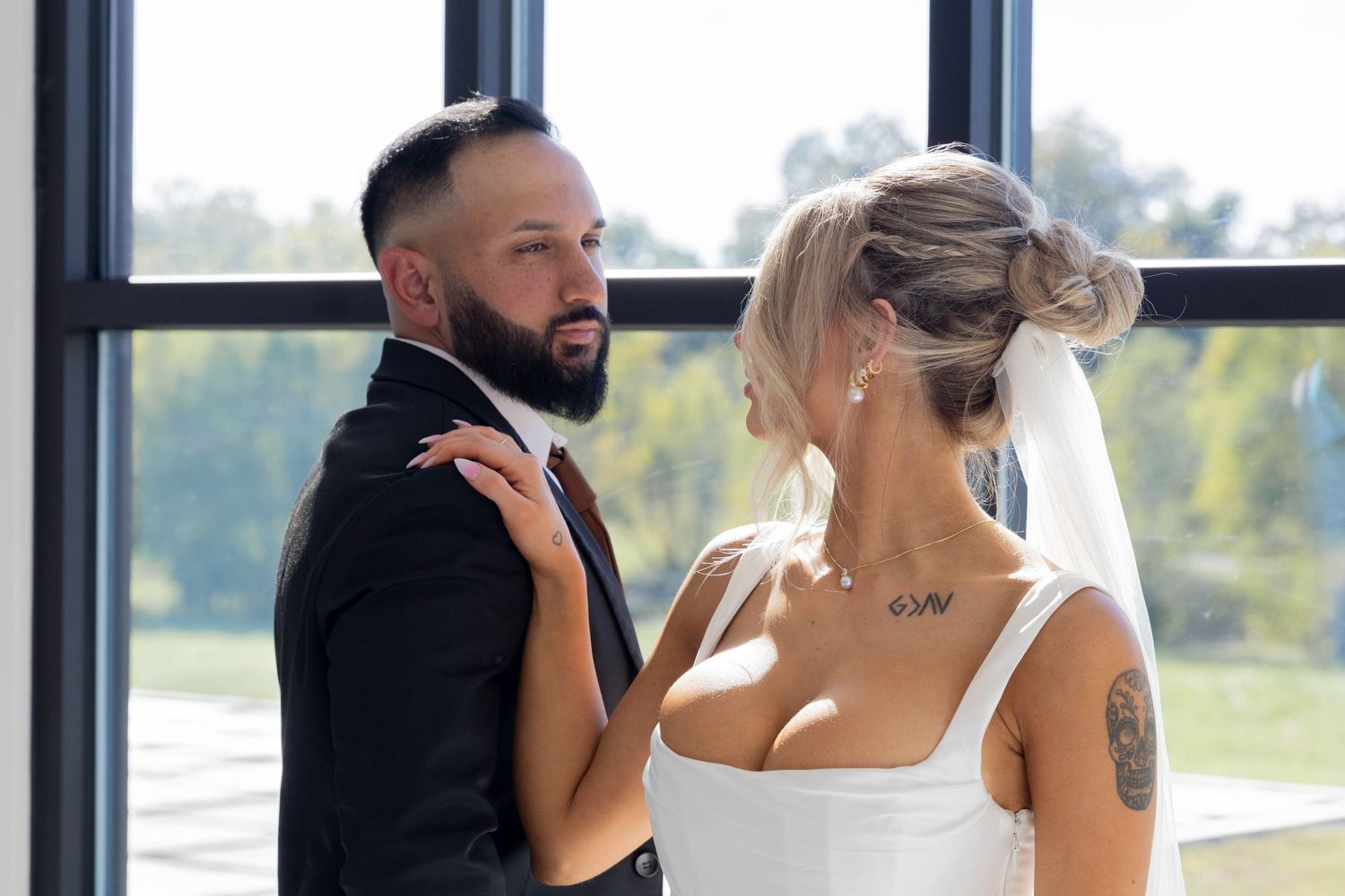 A couple shares an intimate moment during their wedding ceremony by large windows.