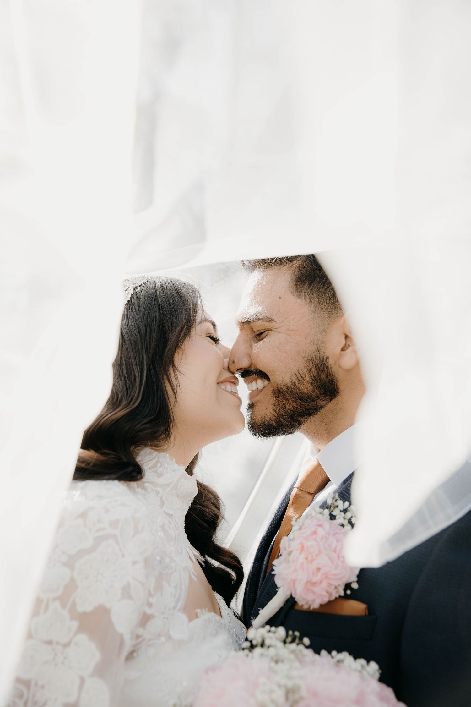 A romantic wedding moment captured through sheer white fabric with a pink floral boutonniere detail.