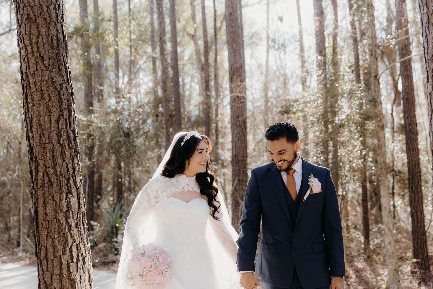 Wedding couple walks hand in hand through a serene forest path lined with tall pine trees on their special day.