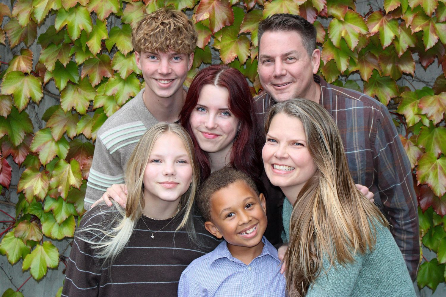 A joyful family of six poses together in front of a colorful autumn ivy wall.