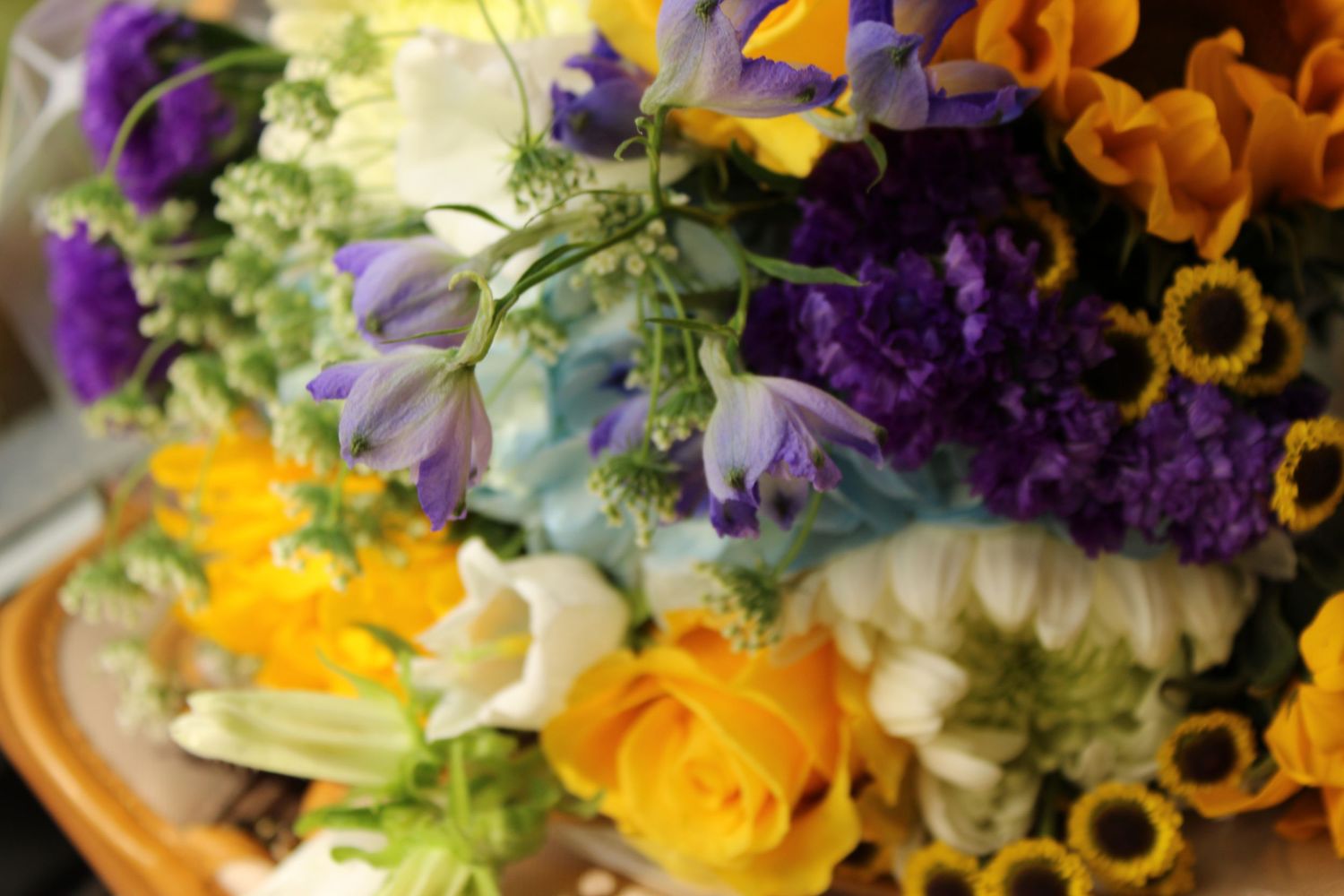 Colorful floral arrangement with purple statice, yellow roses, blue bells, and sunflowers for a wedding bouquet.