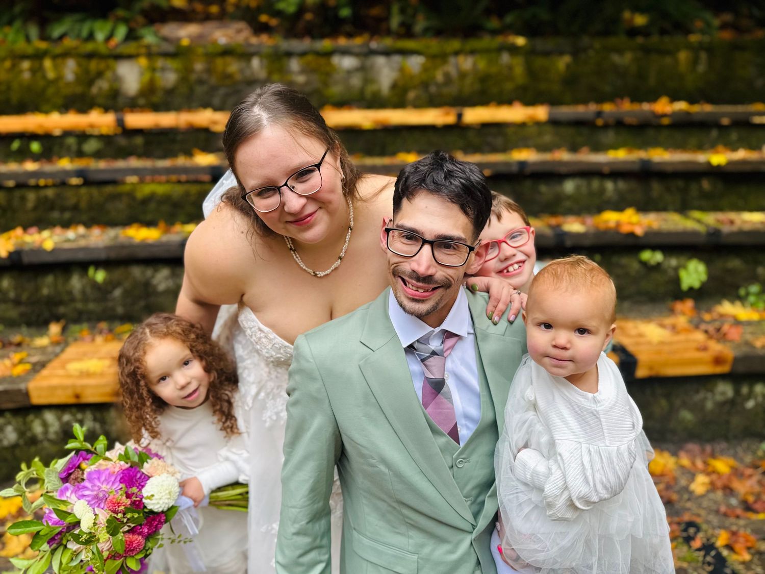 Happy family of four posing together at autumn outdoor wedding ceremony.
