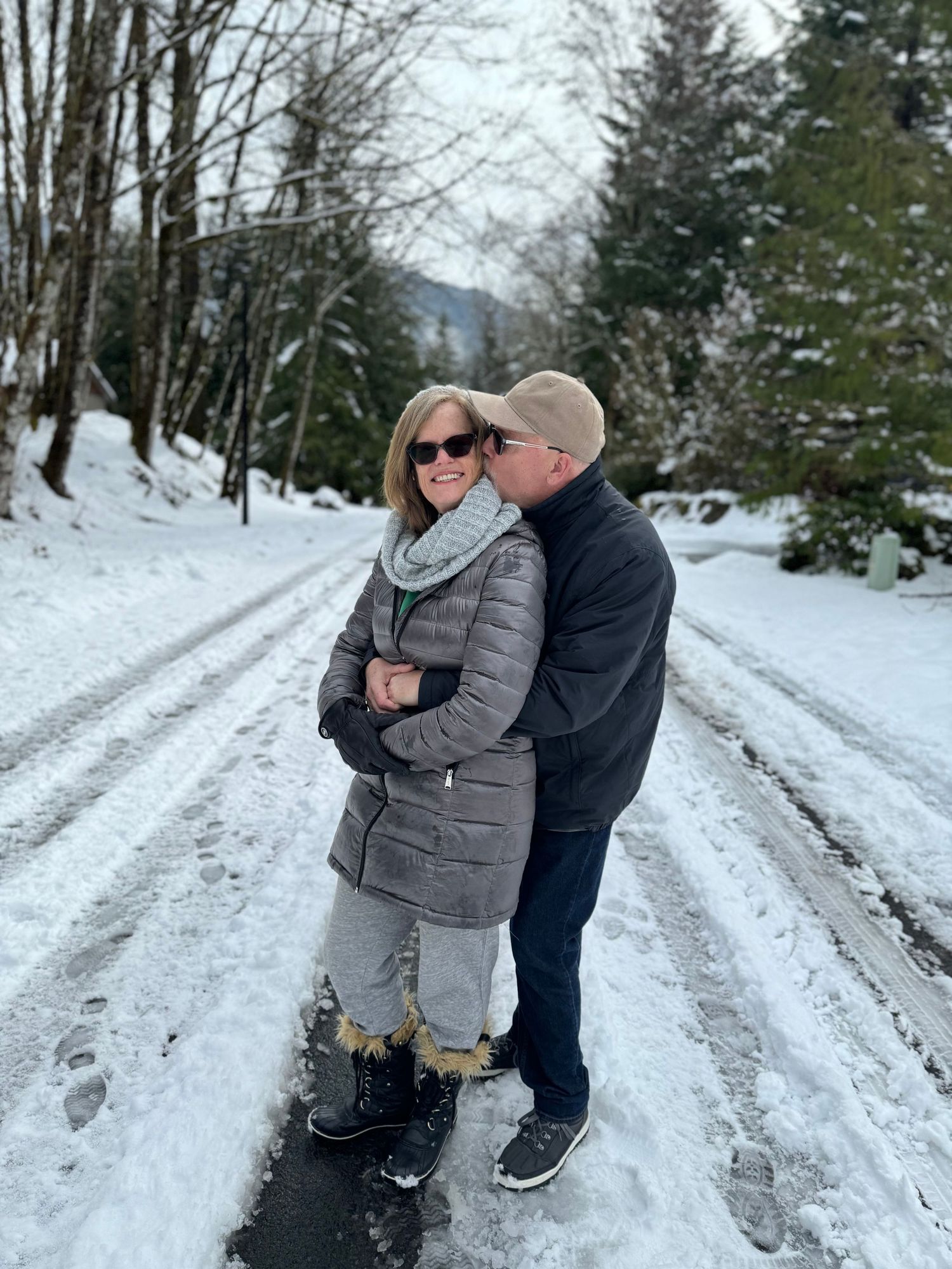 Couple embracing on a snowy road surrounded by winter trees.
