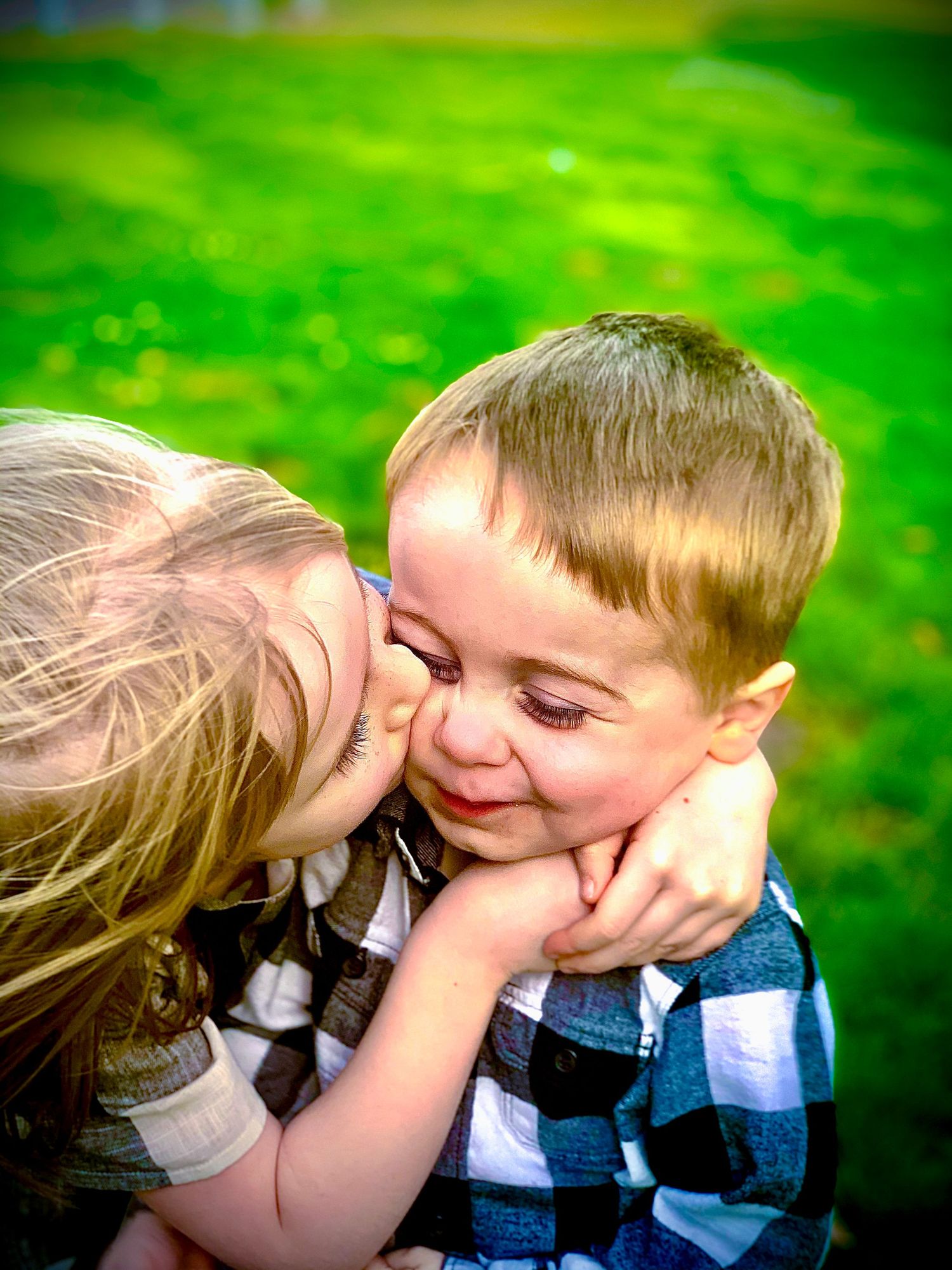 Sweet young girl giving a kiss on the cheek to a smiling little boy on a green grass background.