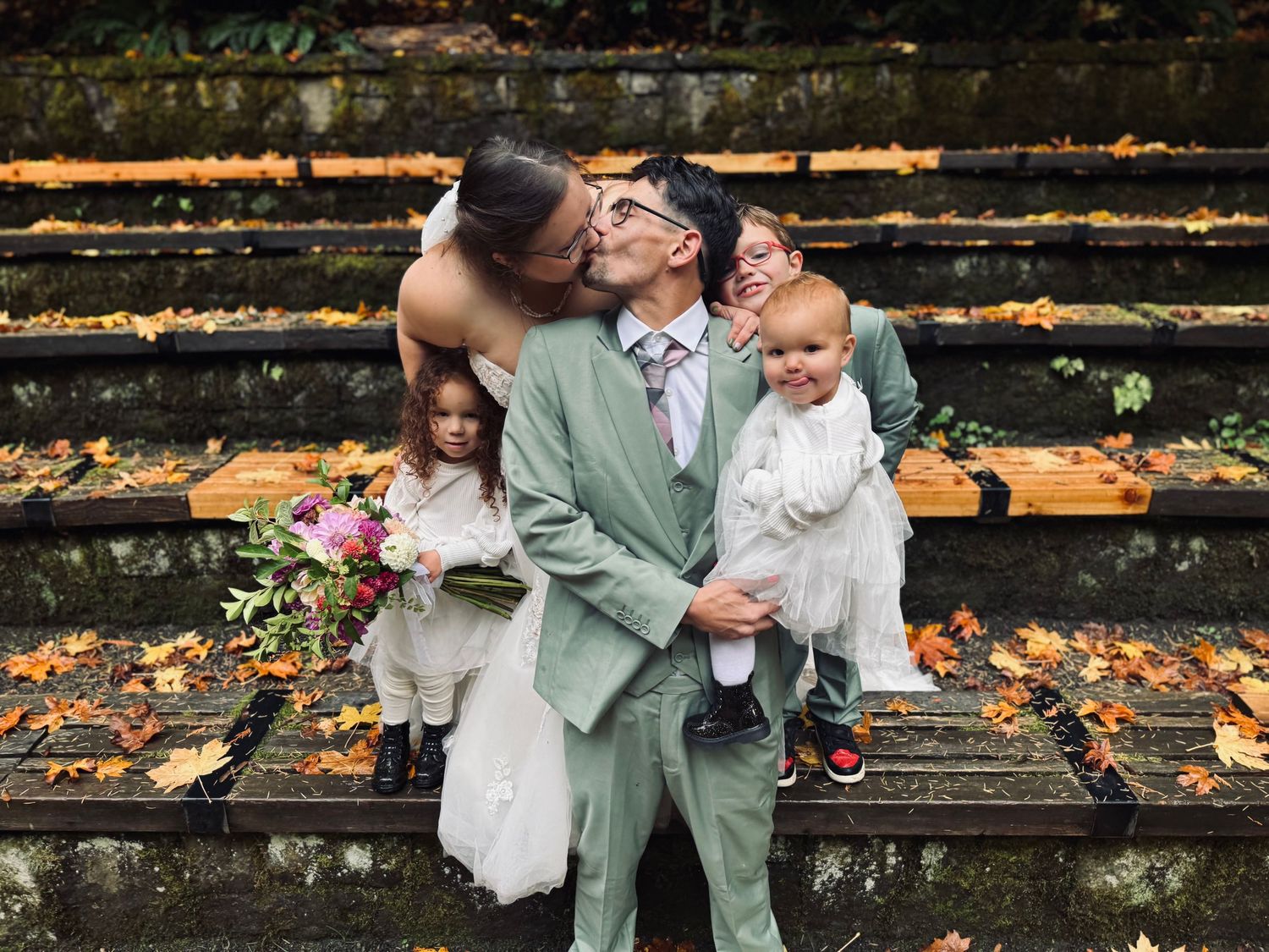 Wedding family portrait with bride and groom kissing on autumn stone steps.