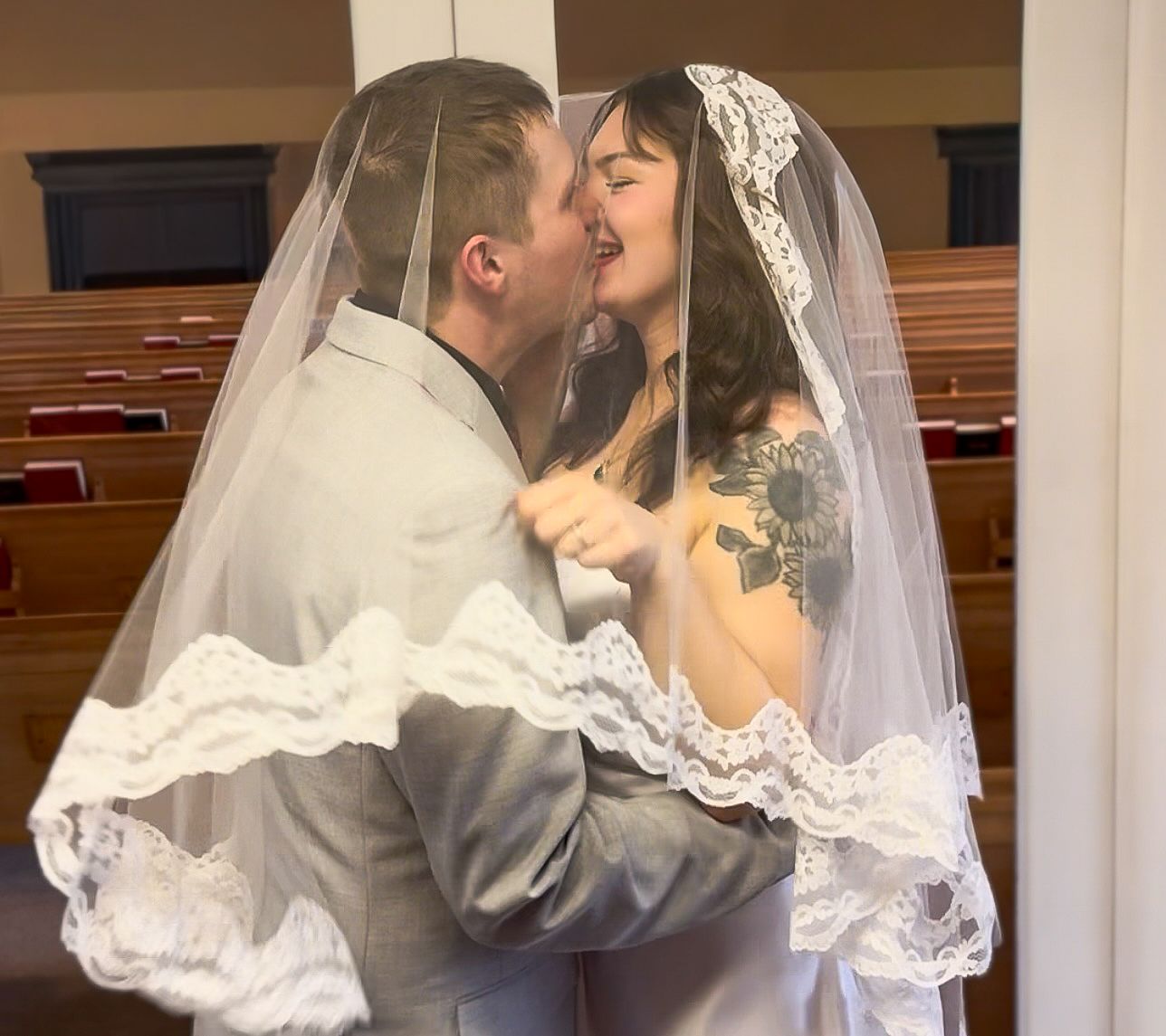 A groom lifts and kisses his bride in a lace veil during their wedding ceremony inside a church.