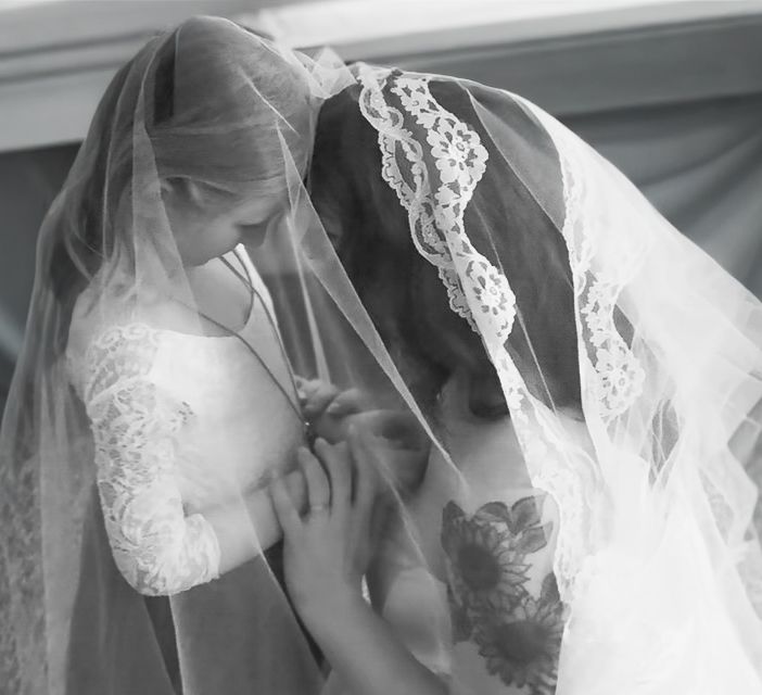 A black and white photo of two women in wedding veils sharing a quiet emotional moment together.