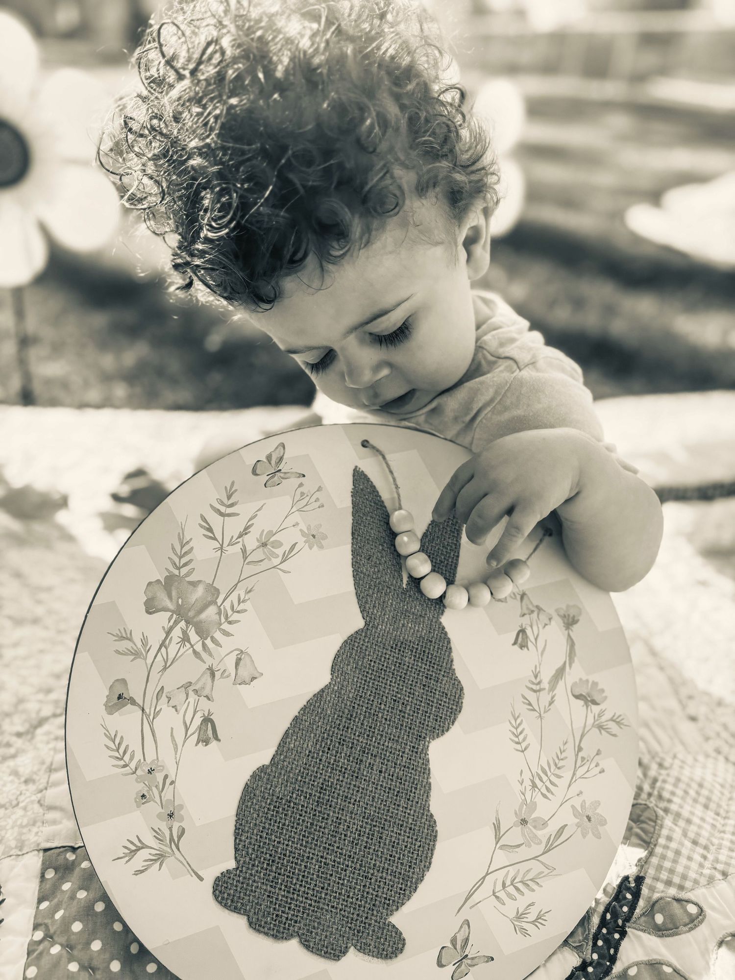 Curly-haired toddler examining Easter bunny decorative plate outdoors in sepia tone.