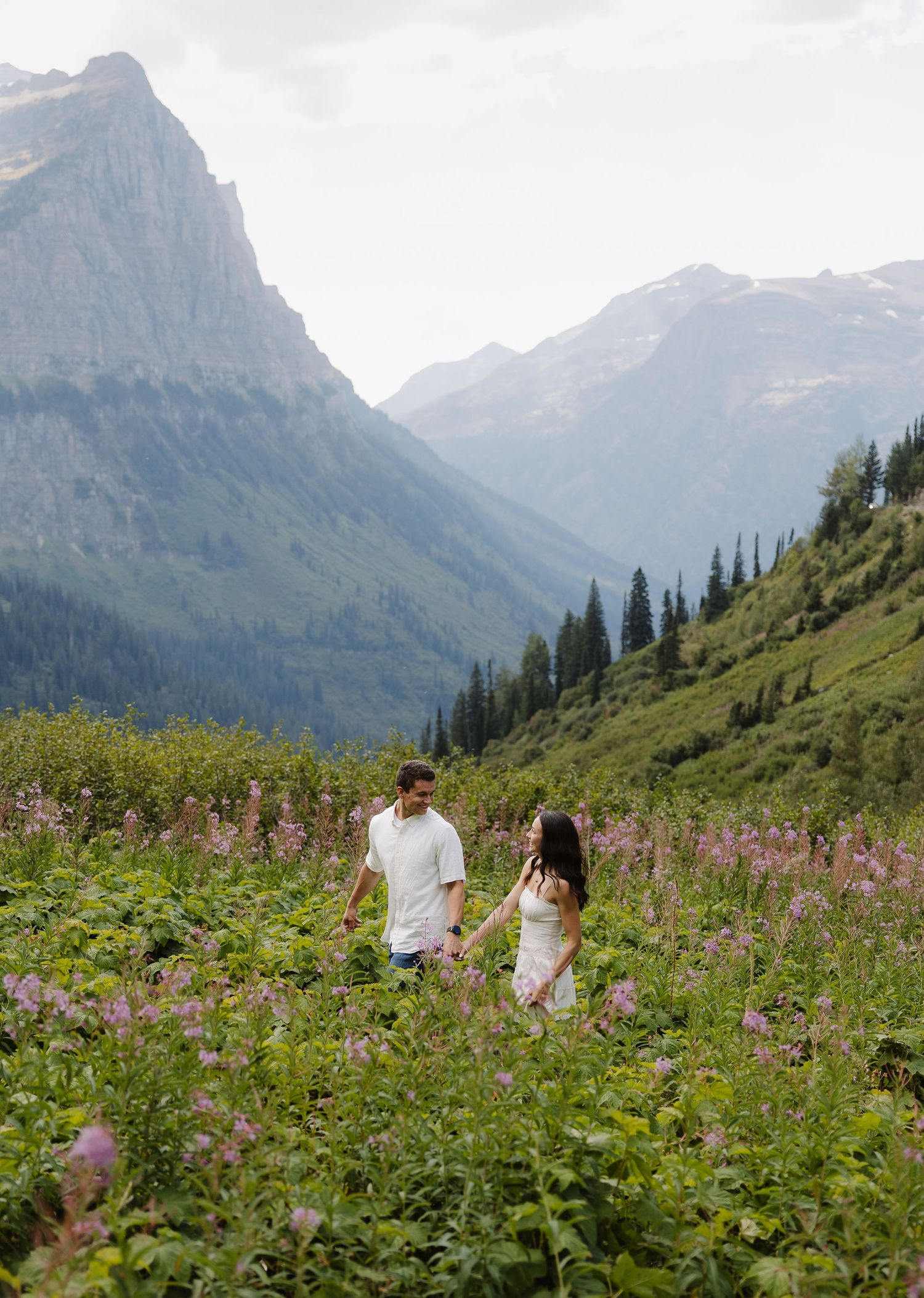 Couple holding hands walking through purple wildflowers in scenic mountain valley.