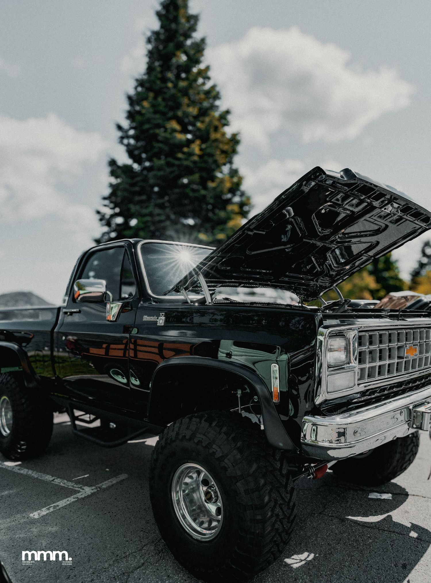 Black lifted Chevrolet square-body truck with open hood at car show.