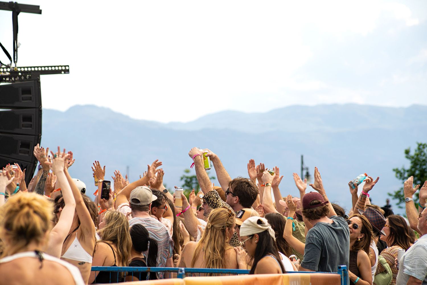 Crowd of festival-goers with hands raised at an outdoor music festival with mountain views.