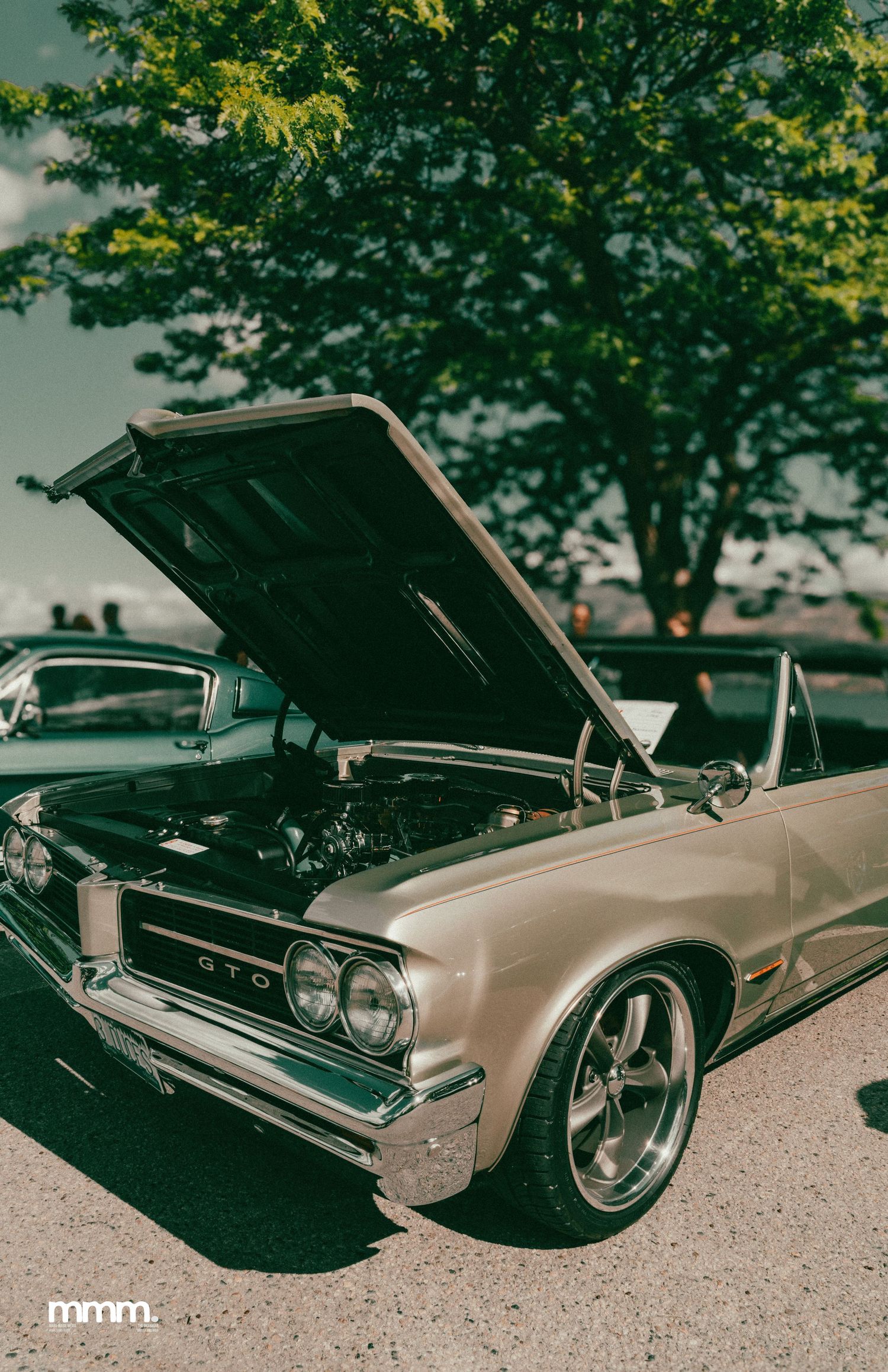 Silver classic Pontiac GTO convertible with hood open displayed at outdoor car show.