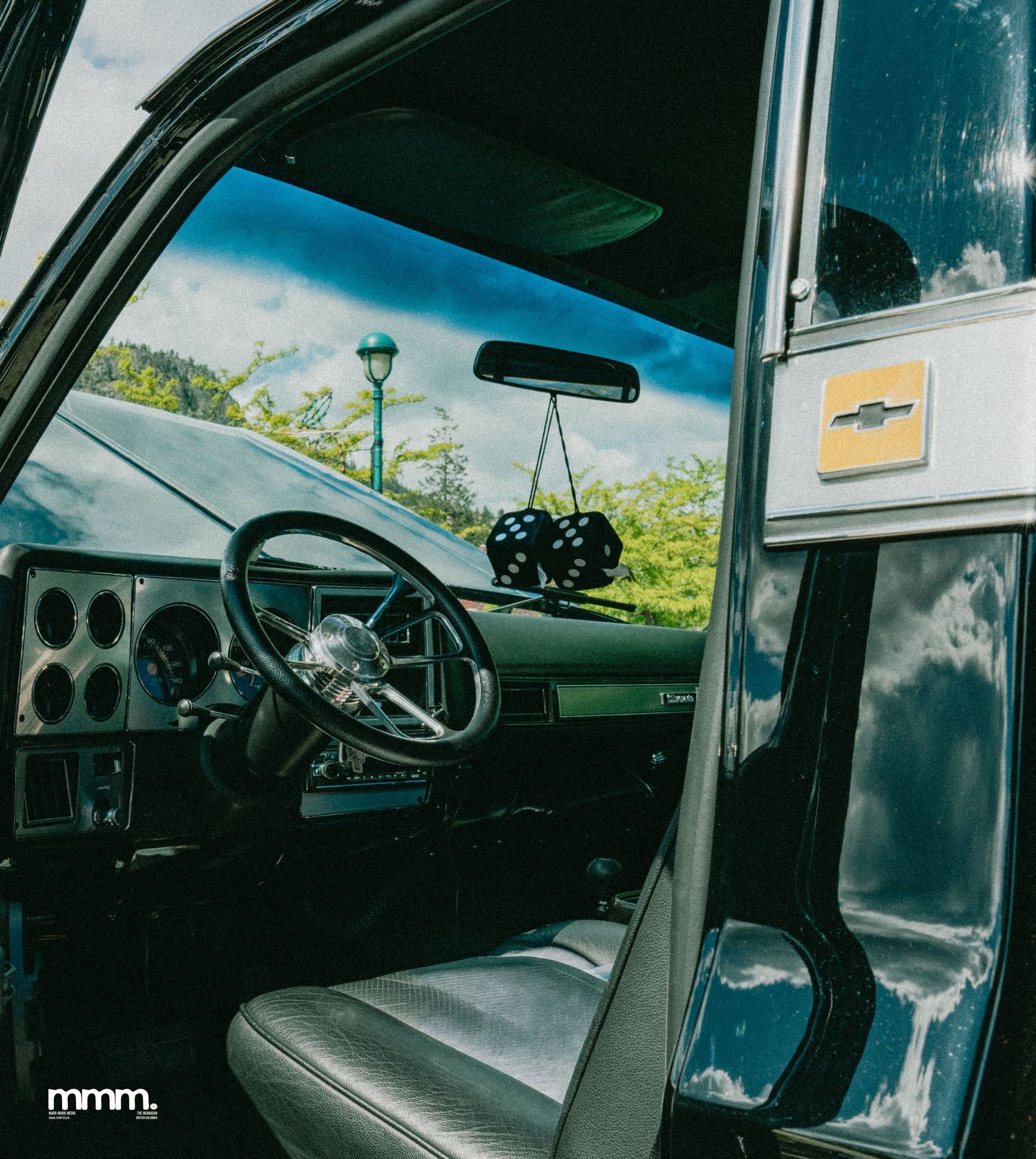 Chevrolet truck interior with fuzzy dice and blue sky reflection.
