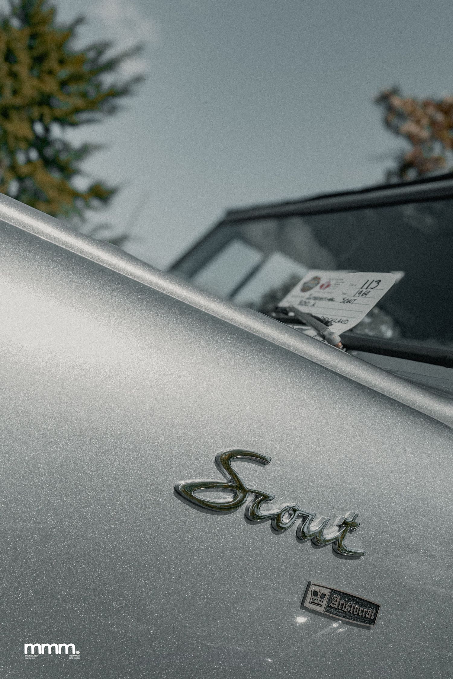 Silver International Scout badge on hood at outdoor car show.