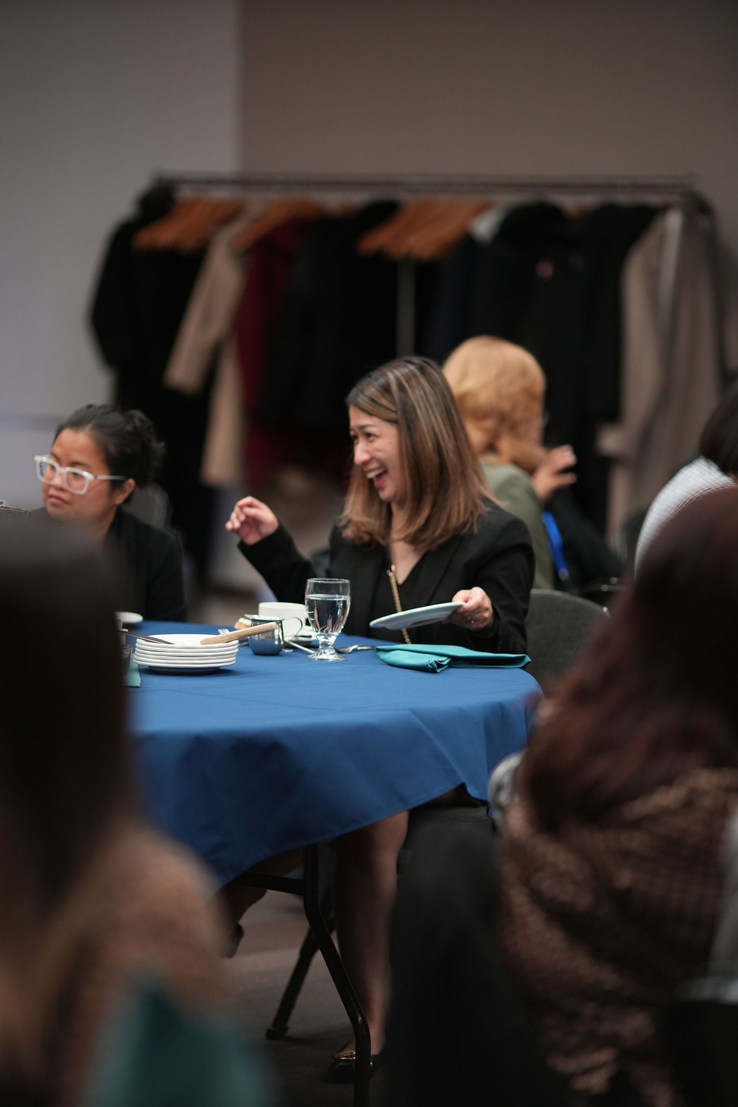 Woman laughing joyfully at a blue-tablecloth dinner table during a professional networking event.