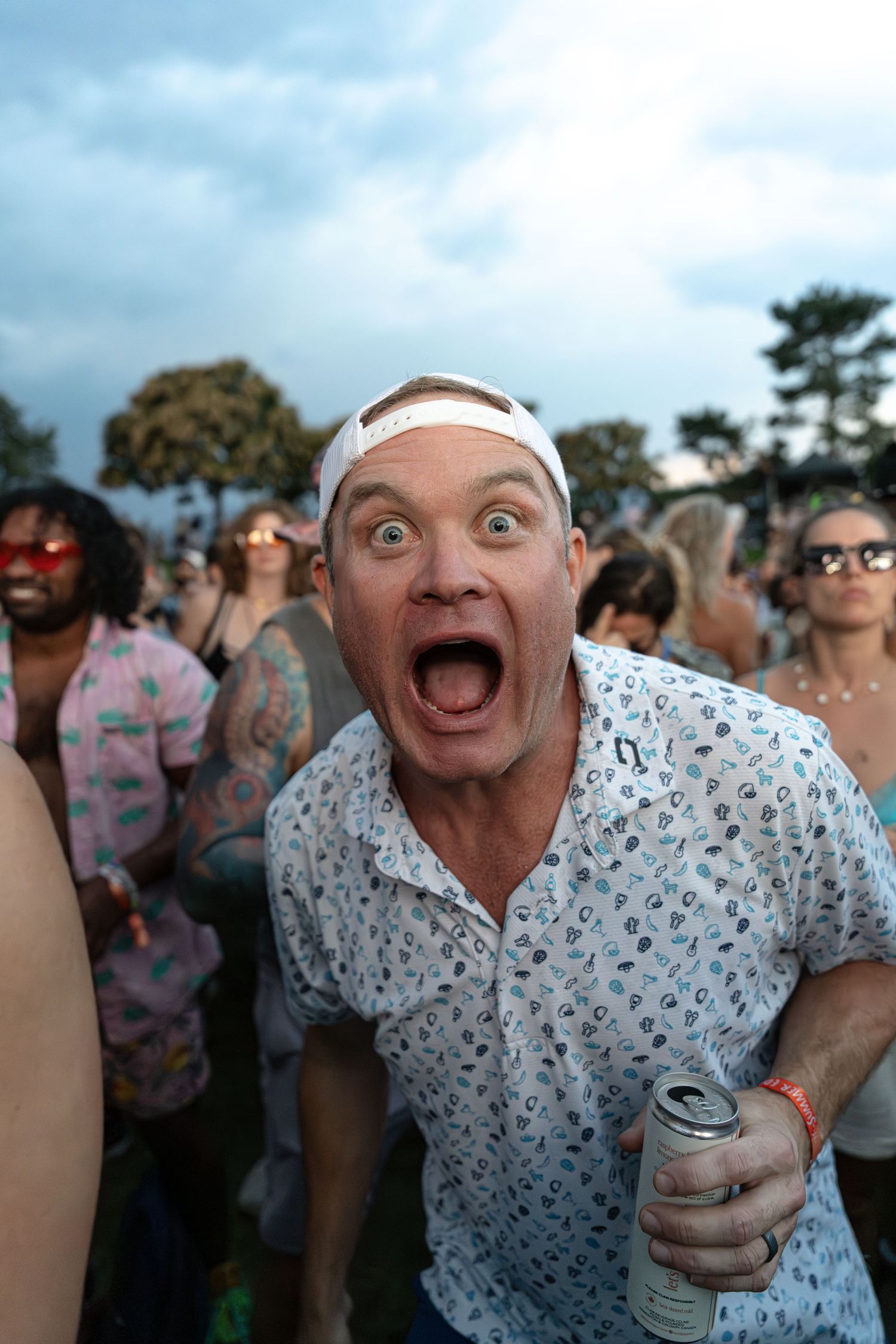 Excited man with wide open mouth holding a drink can at a lively outdoor music festival.