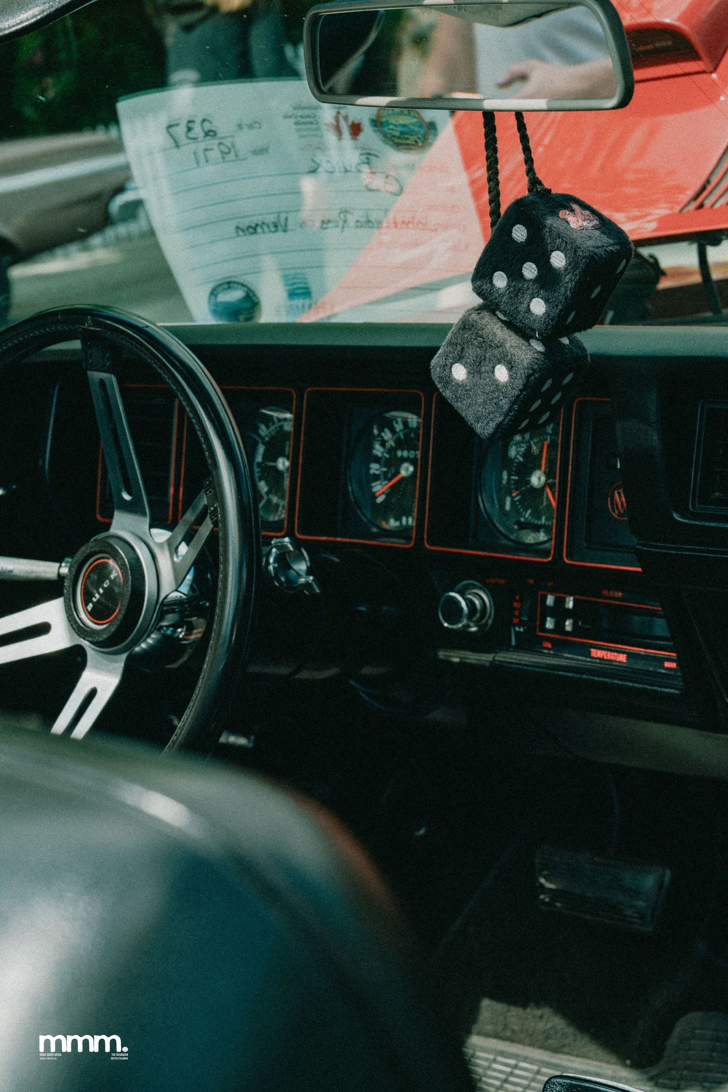 Classic car interior with fuzzy dice hanging from rearview mirror and vintage dashboard.
