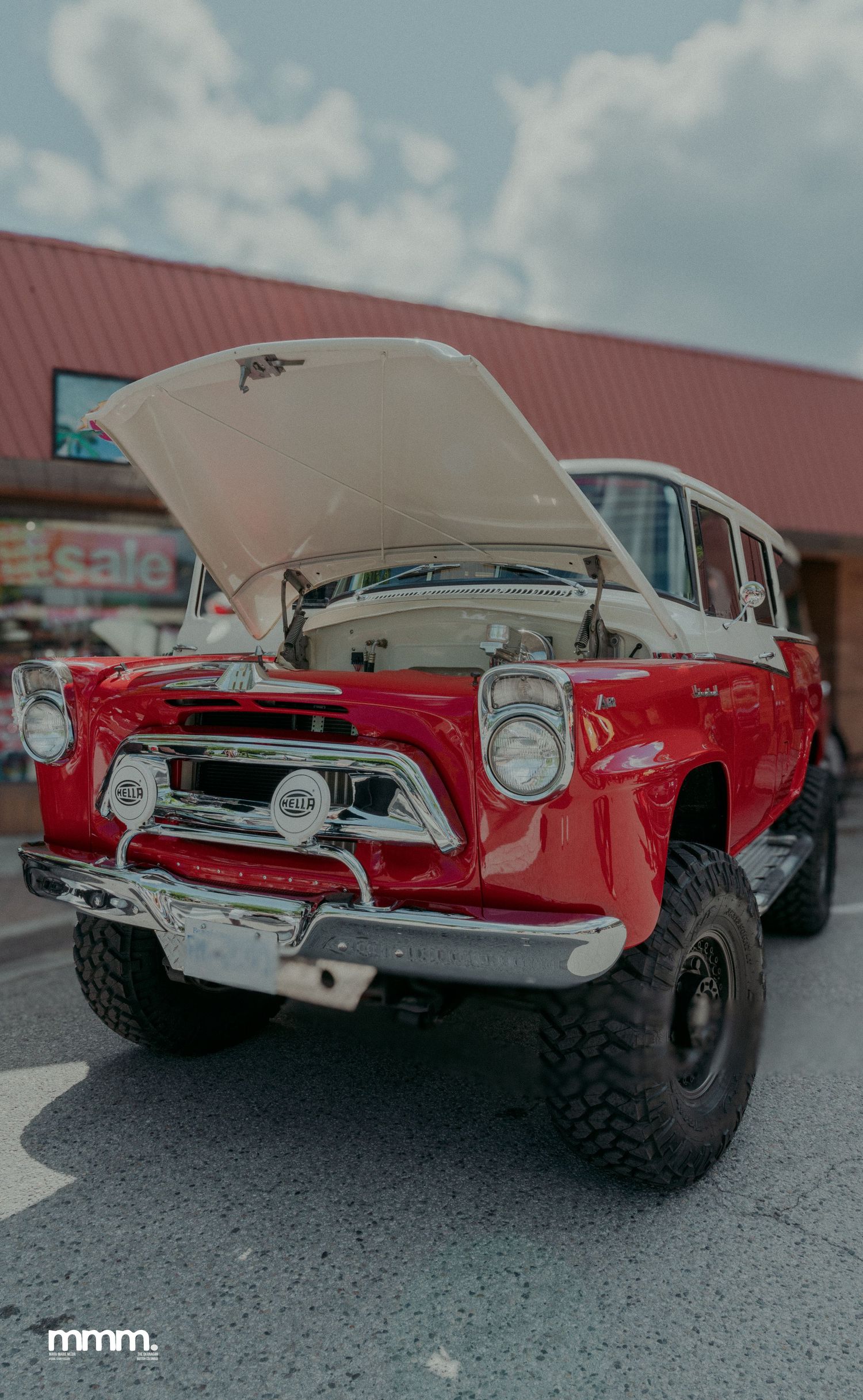 Restored red and white vintage International Scout SUV with hood open at car show.