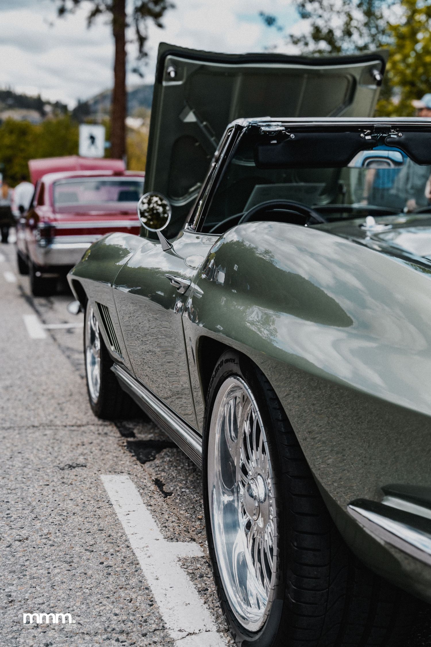 Green classic Corvette convertible with chrome wheels at a car show.