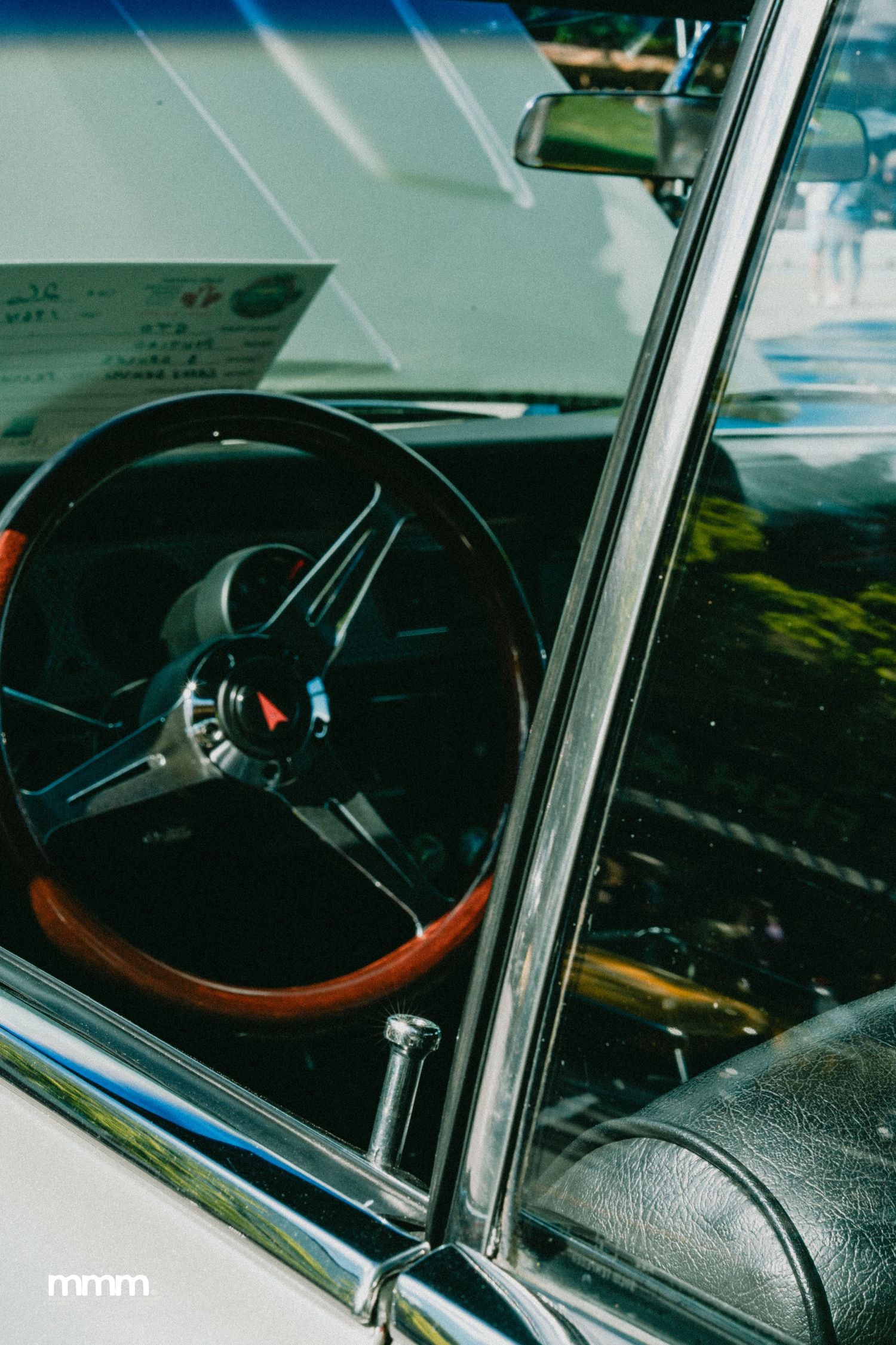 Classic car interior showing wood-grain steering wheel with Pontiac emblem through window.