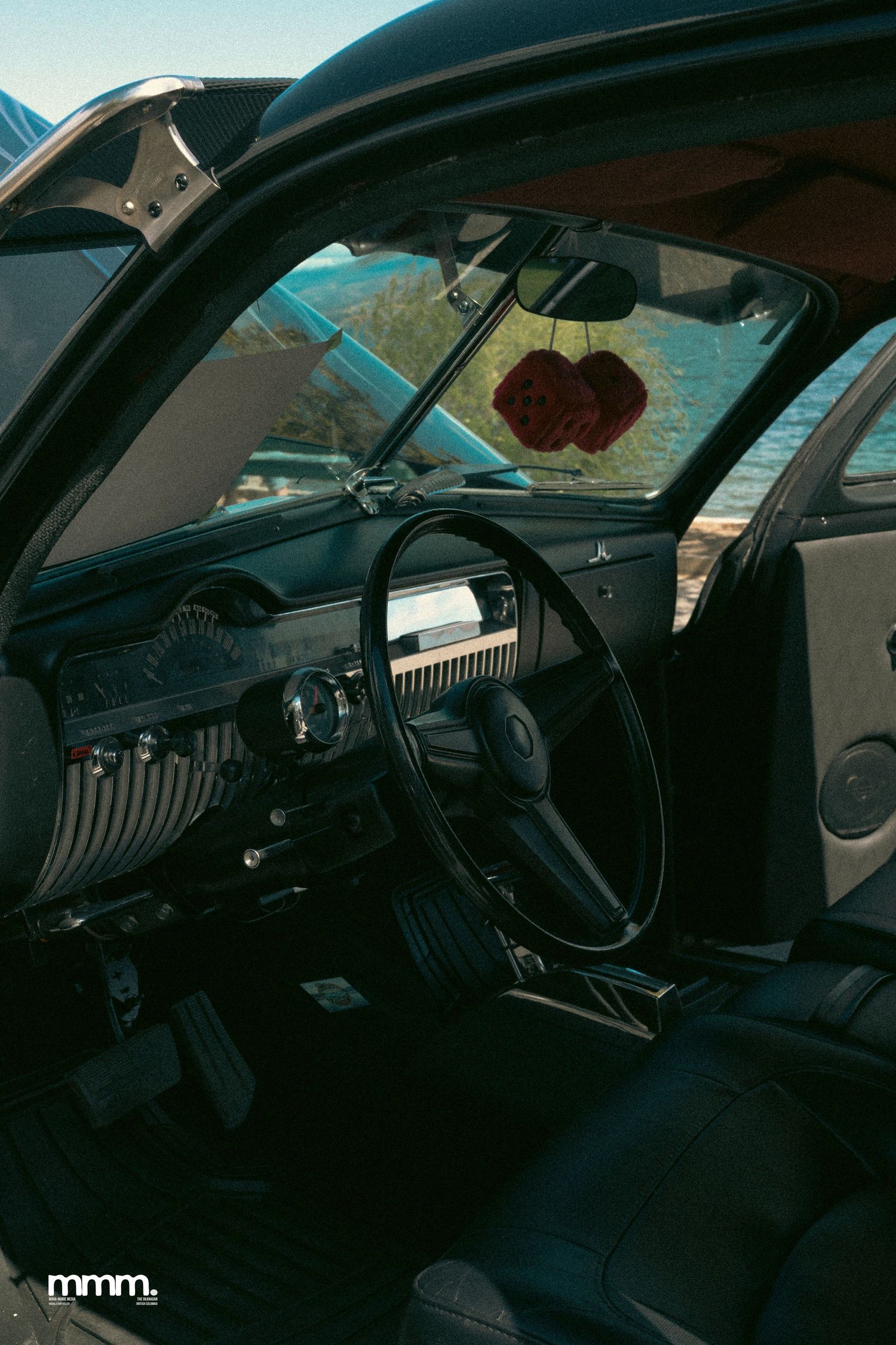 Vintage black car interior with red fuzzy dice hanging from mirror.