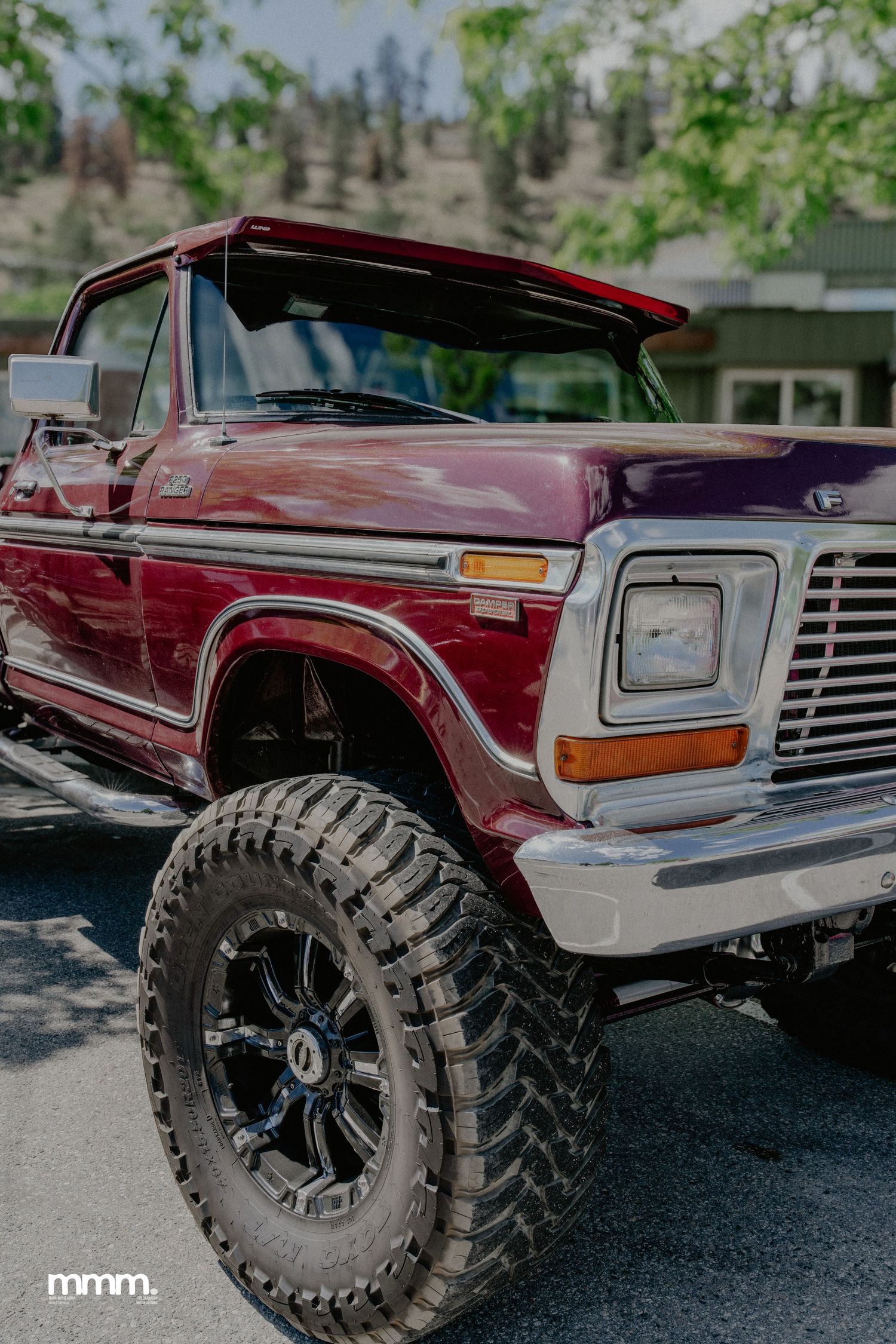Lifted burgundy classic Ford Bronco with oversized mud tires parked outdoors.