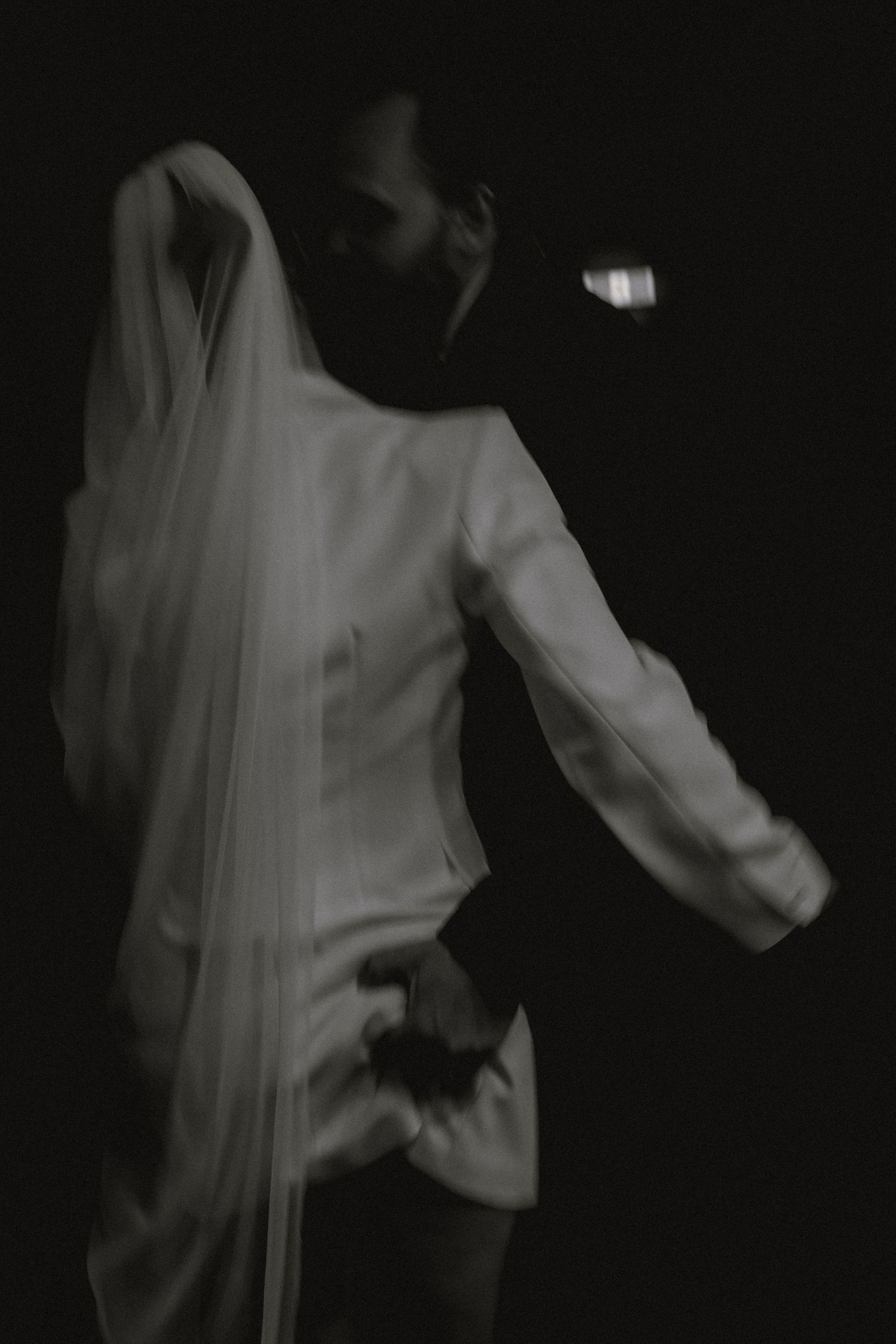 Blurred black and white artistic photo of bride and groom embracing in dramatic dark lighting.
