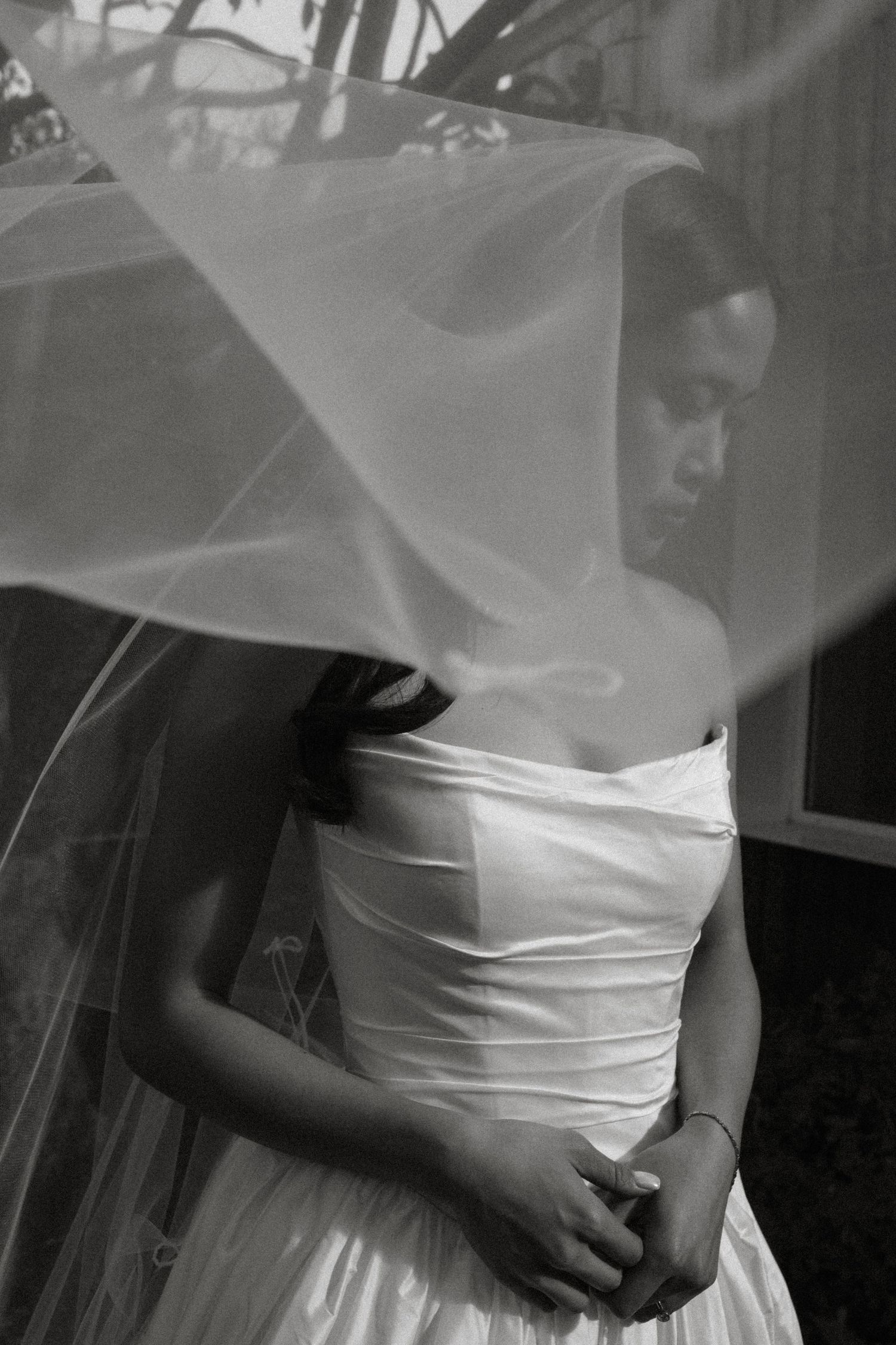 Black and white photo of a bride in a strapless gown with her veil billowing around her face.