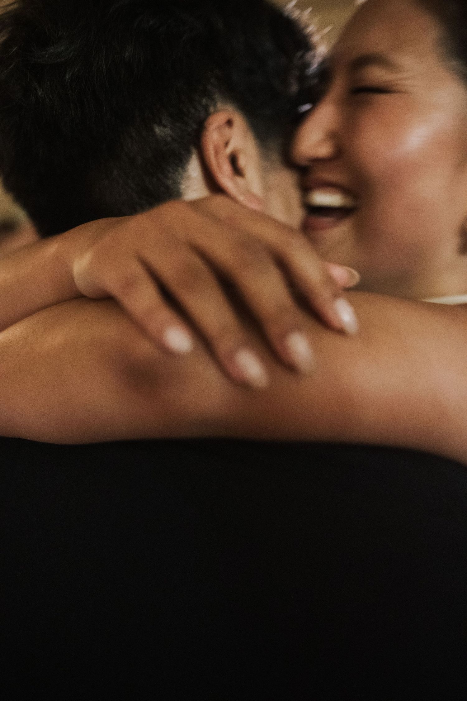 Joyful bride laughs while embracing groom, her hand resting on his shoulder at wedding reception.