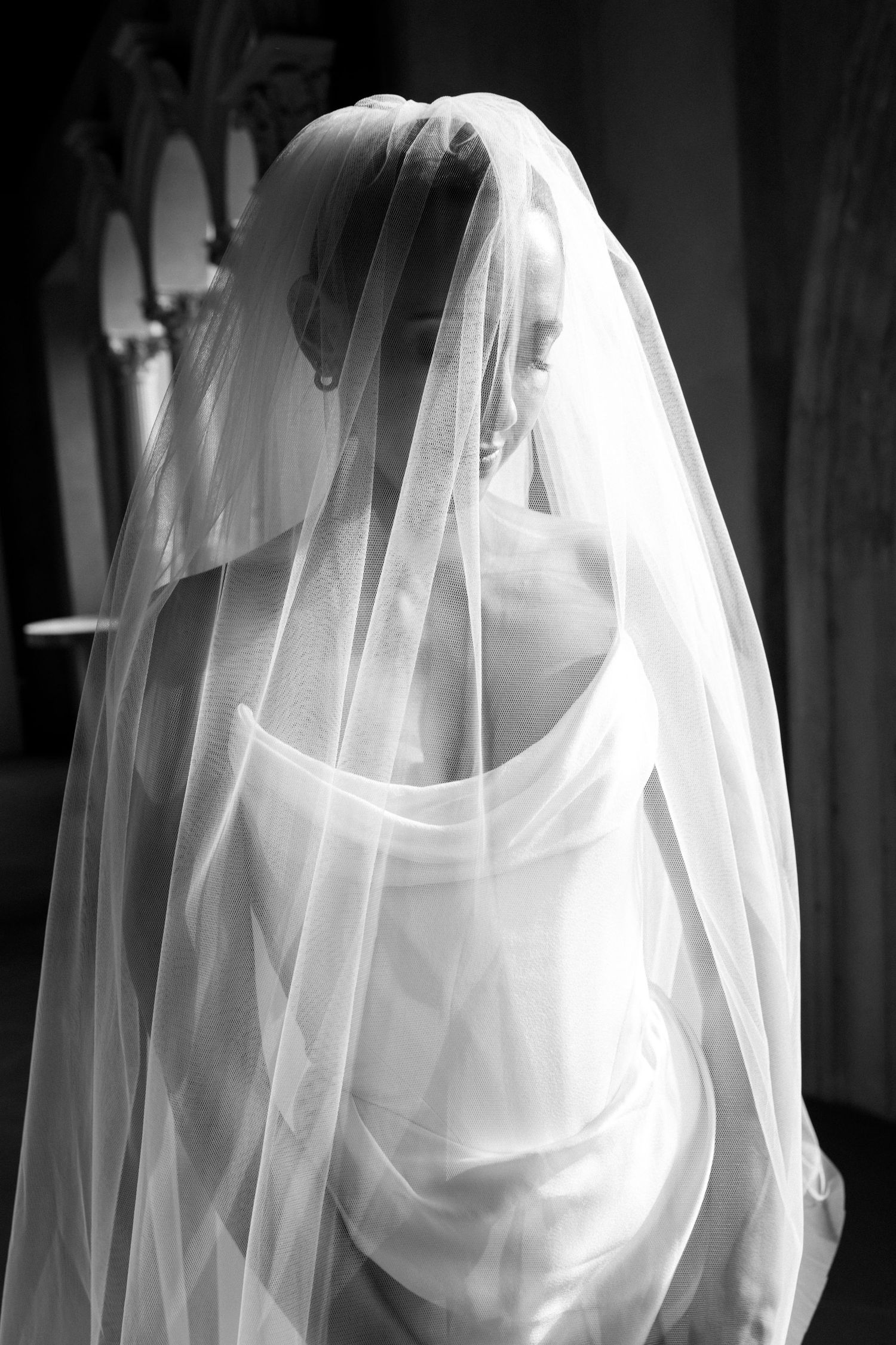 Elegant bride draped in flowing white veil in dramatic black and white wedding portrait.