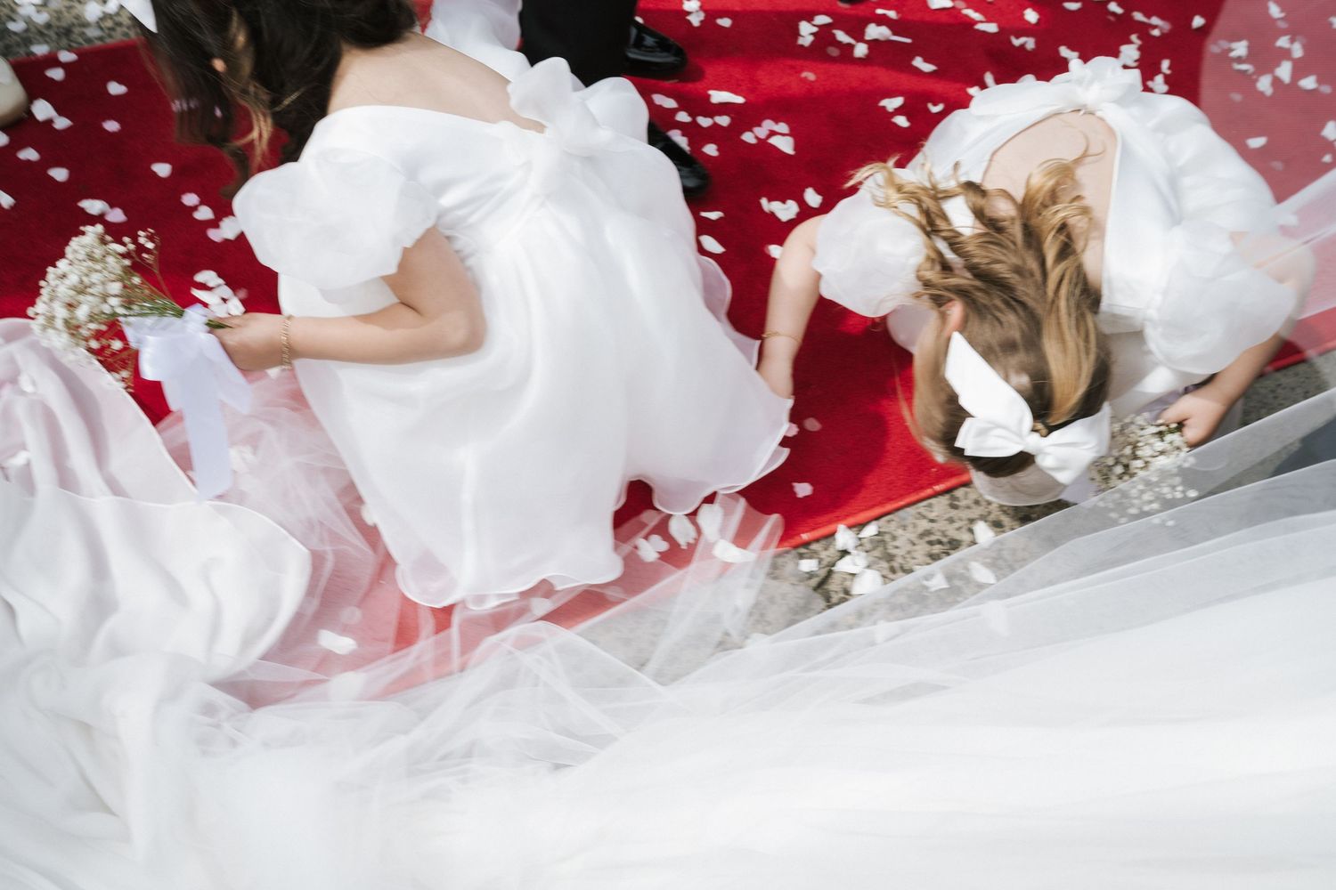 Aerial view of bride in white gown and flower girl surrounded by red rose petals on the ground.