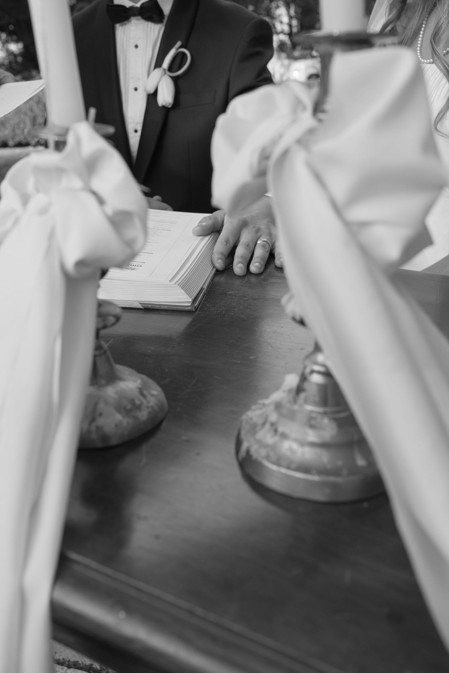 Black and white close-up of groom's hand resting on a book at a wedding ceremony altar.