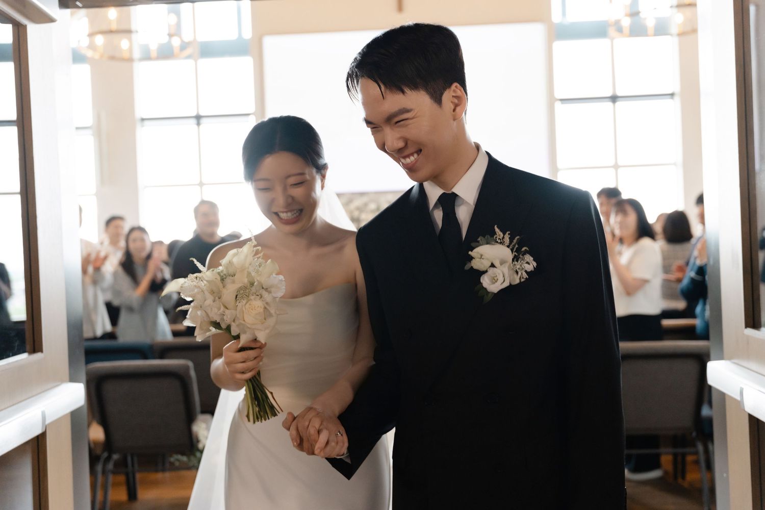 Smiling Asian bride and groom walk down the aisle together at their elegant wedding ceremony.