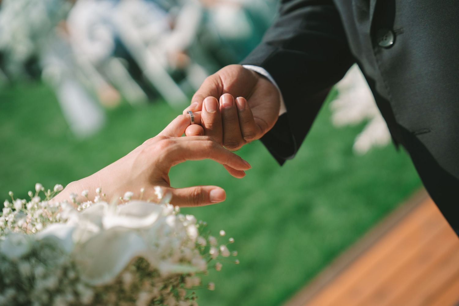 Close-up of groom placing wedding ring on bride's hand during outdoor ceremony.