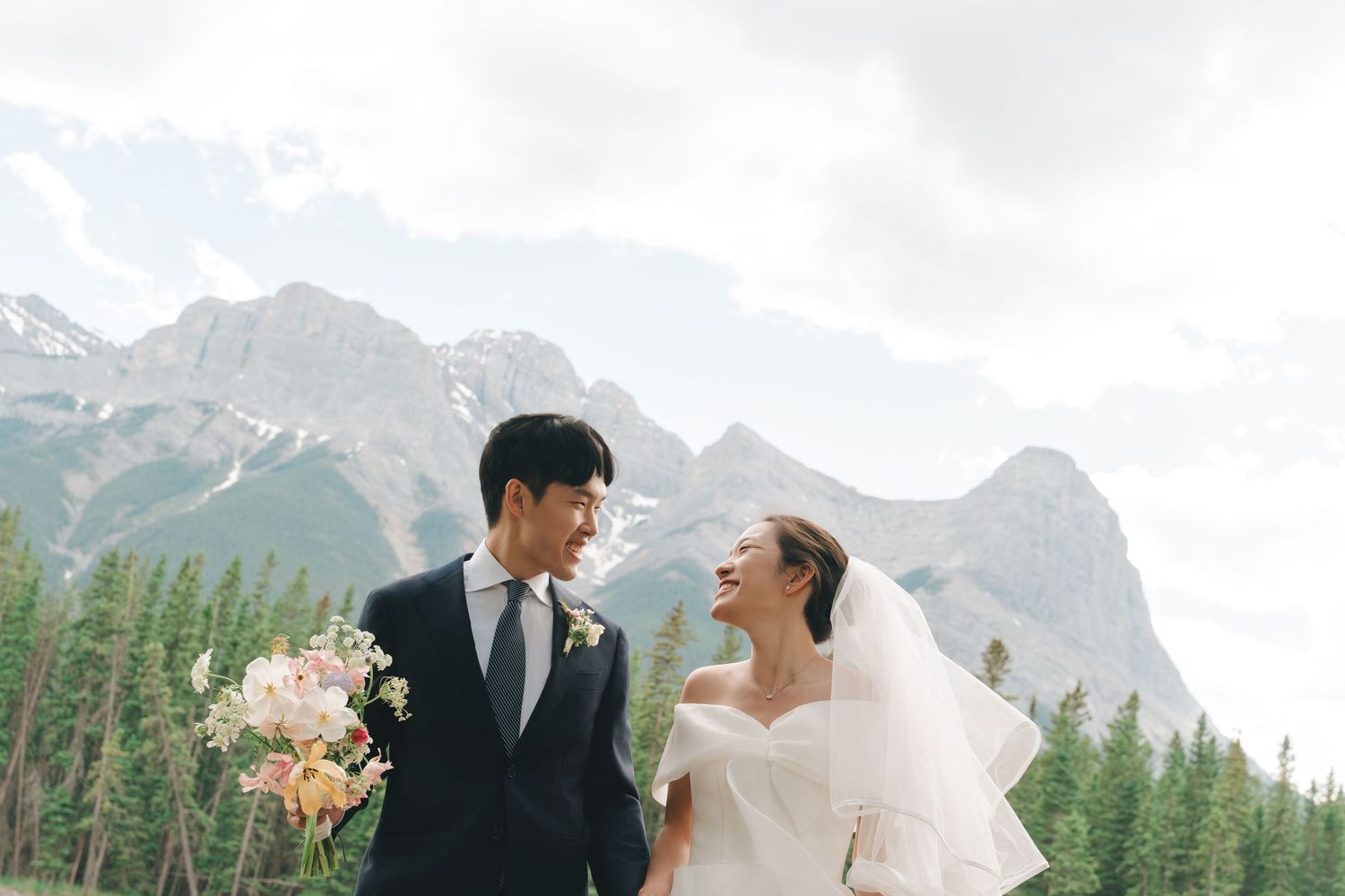 Asian newlyweds share a romantic look with stunning mountain and pine forest backdrop on wedding day.