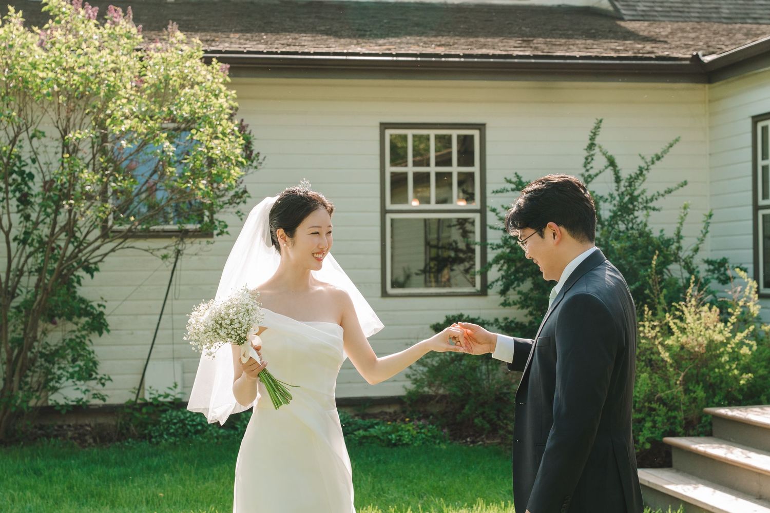 Bride and groom share a tender first look moment holding hands on lush green lawn.