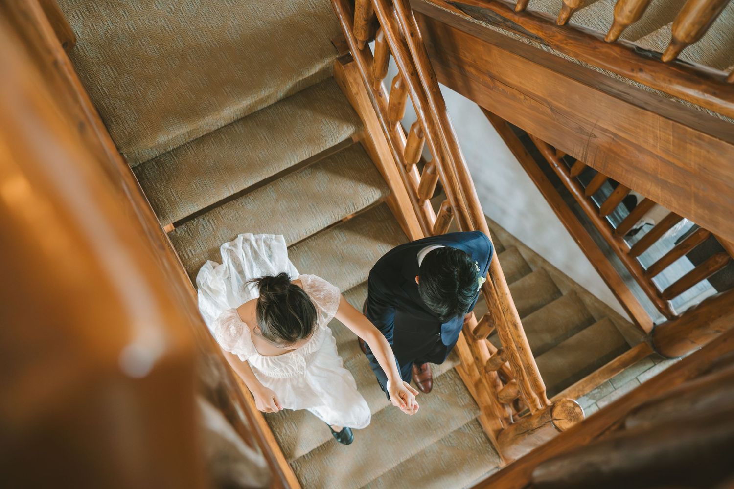 Aerial view of bride and groom holding hands while descending a rustic wooden staircase together.