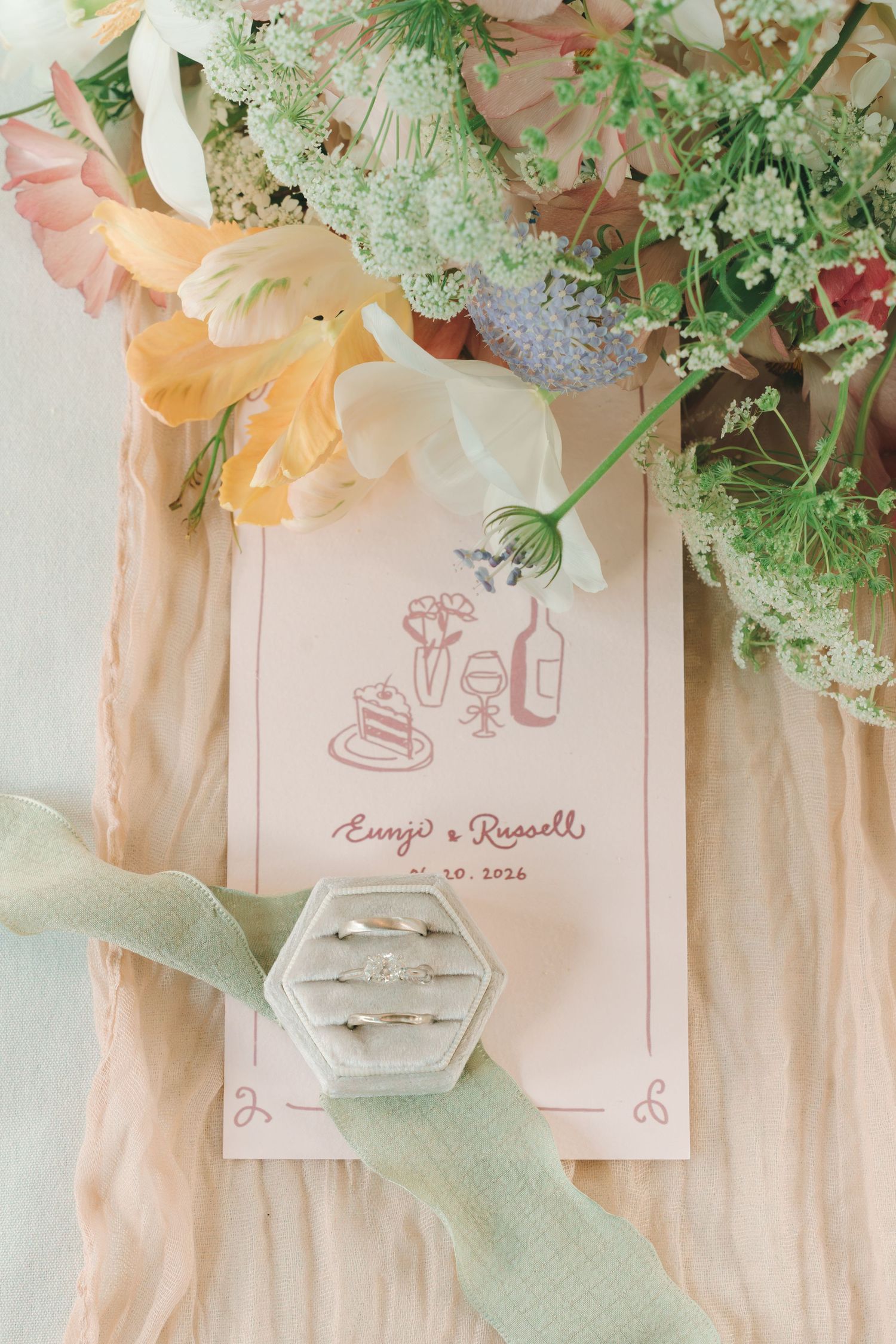 Wedding stationery flat lay featuring rings in a velvet box, floral bouquet, and menu card for Eunji and Russell.