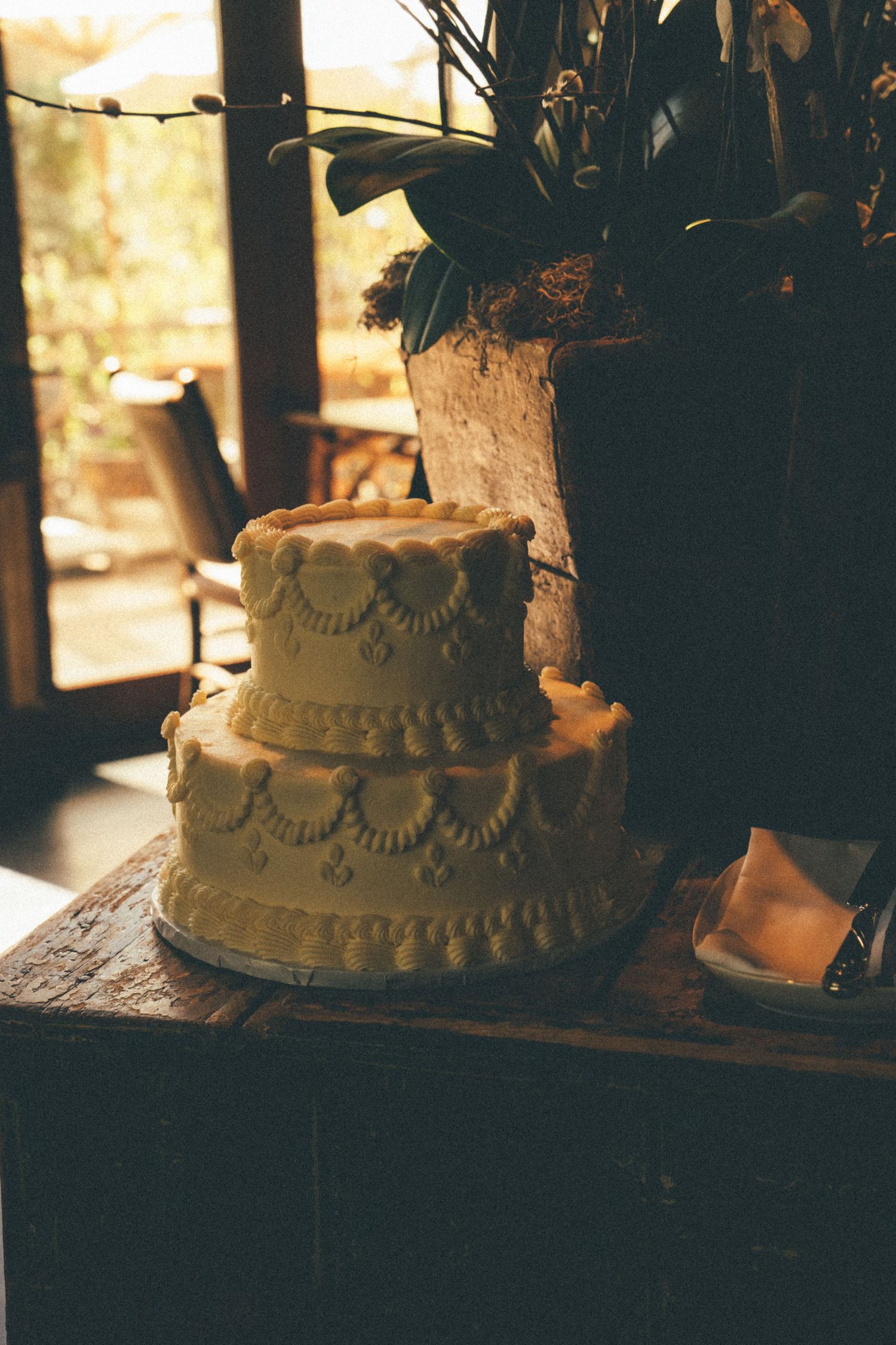 Elegant two-tier white wedding cake with decorative frosting displayed on rustic wooden table.