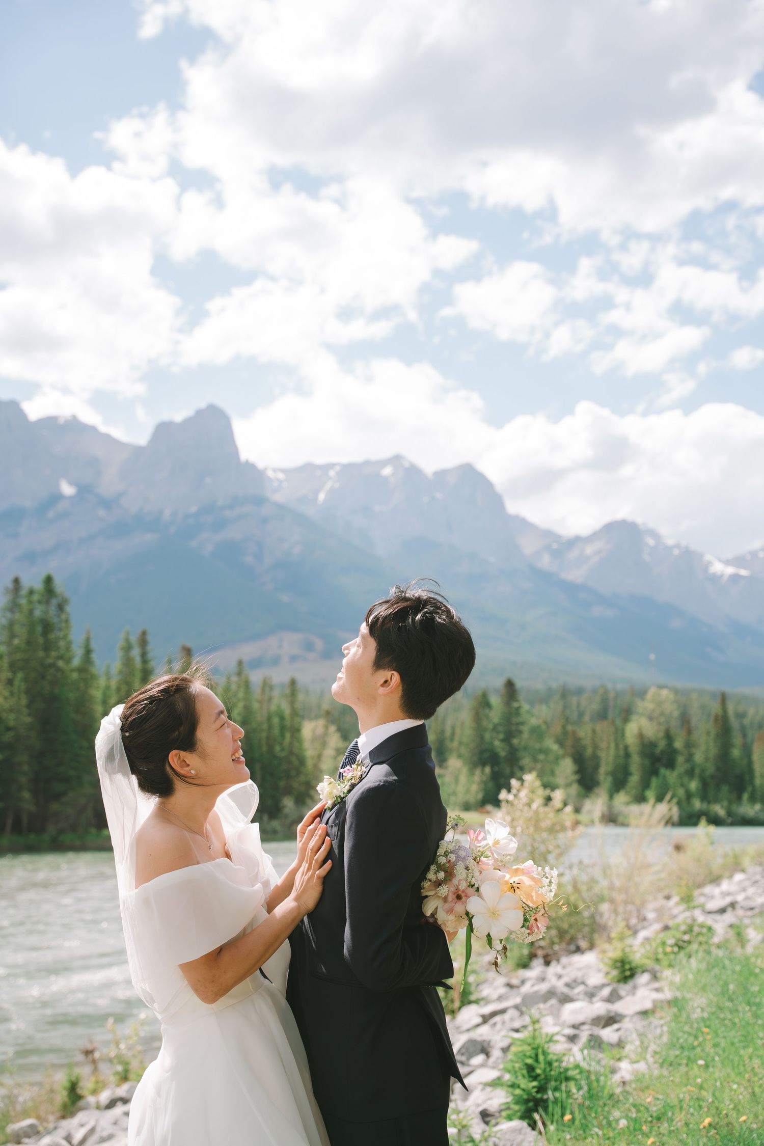 Wedding couple embraces outdoors with stunning Rocky Mountain peaks and evergreen forest behind them.