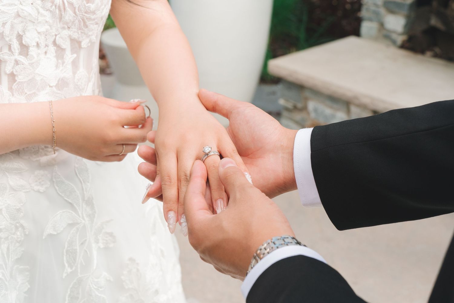 Groom placing a diamond wedding ring on bride's finger during wedding ceremony.