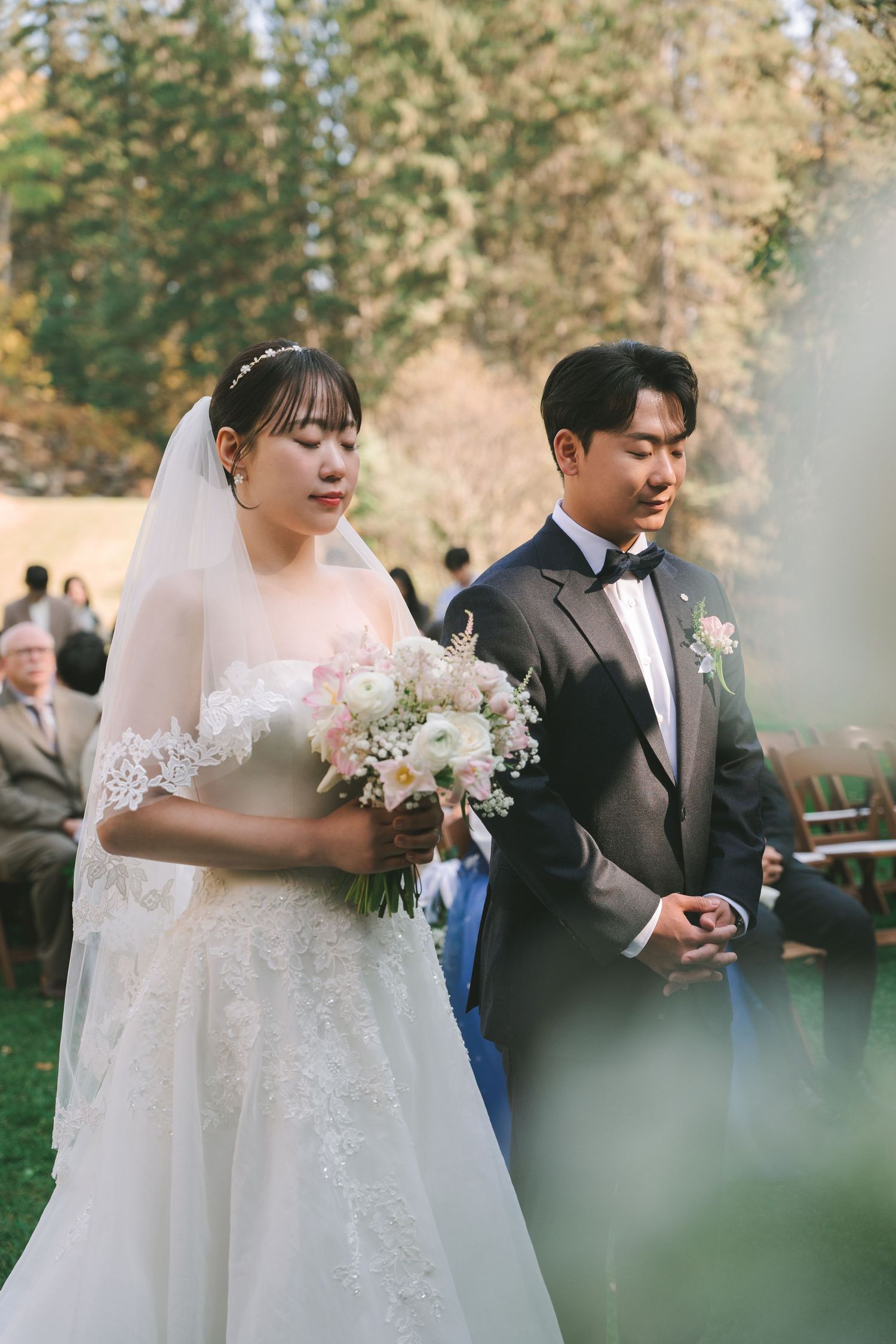 Bride in lace gown and groom in tuxedo walk together during outdoor fall wedding ceremony.
