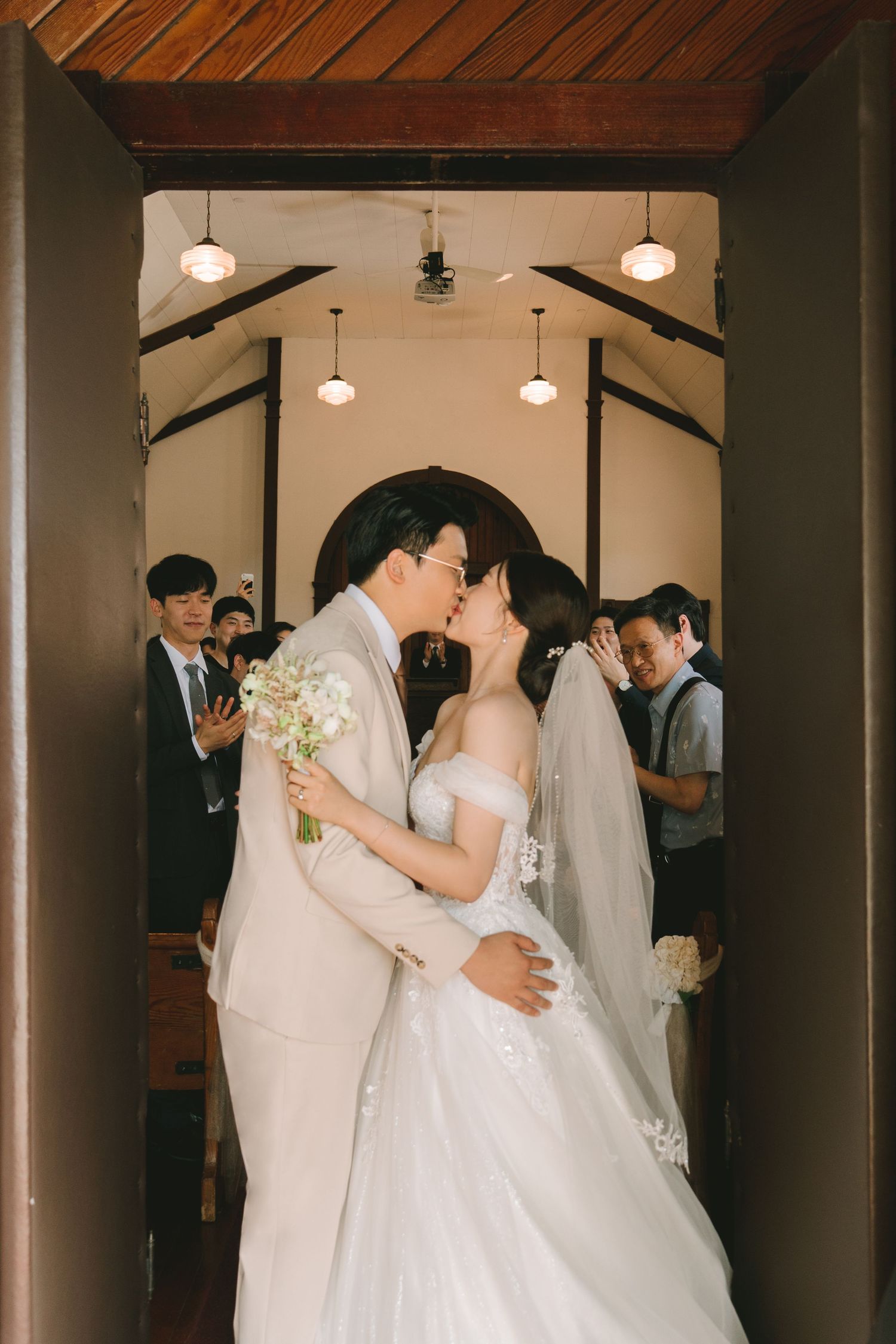 Bride and groom share first kiss at church entrance while guests celebrate their wedding ceremony.