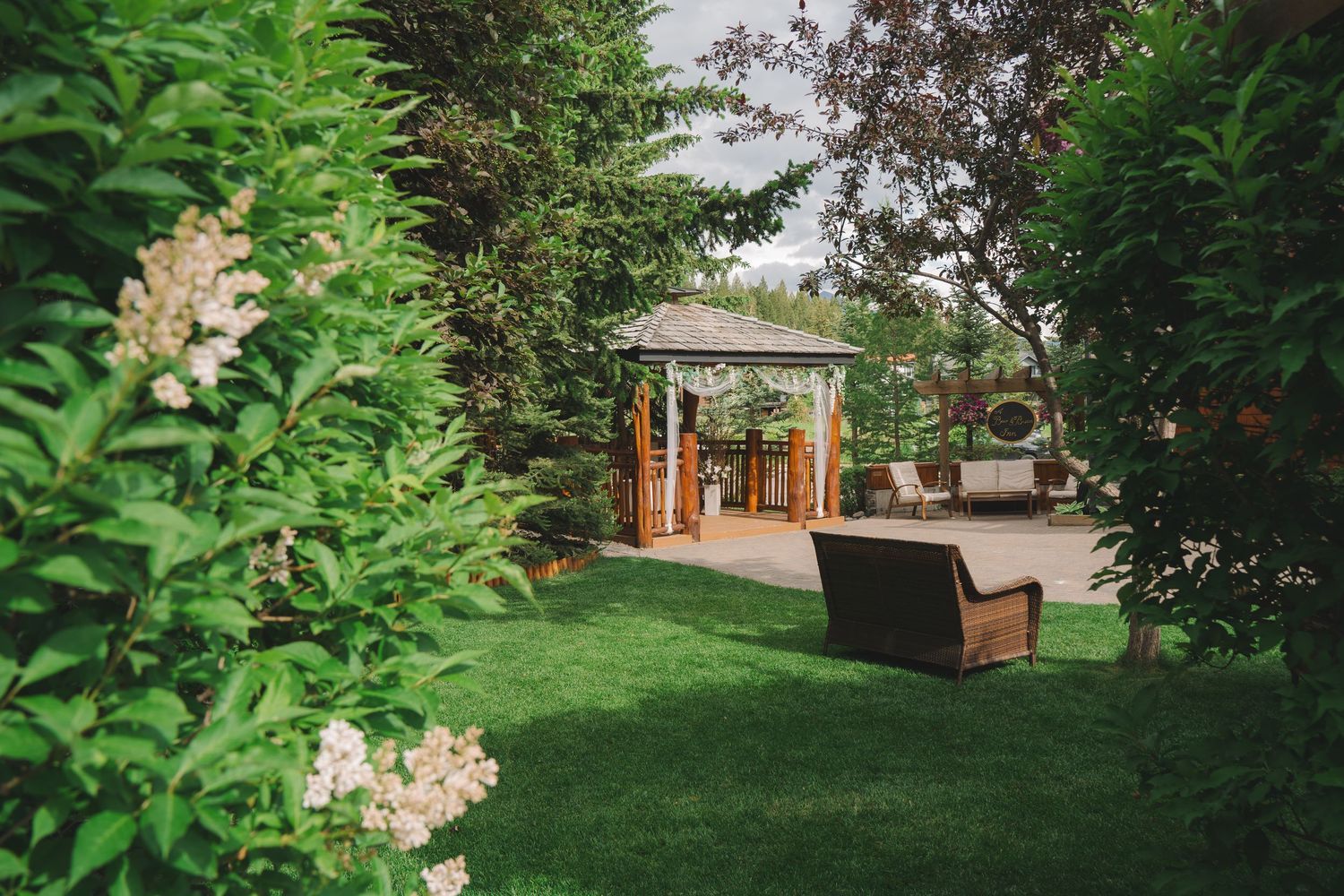 Serene garden wedding venue with lush green lawn, blooming flowers, and a charming wooden gazebo.