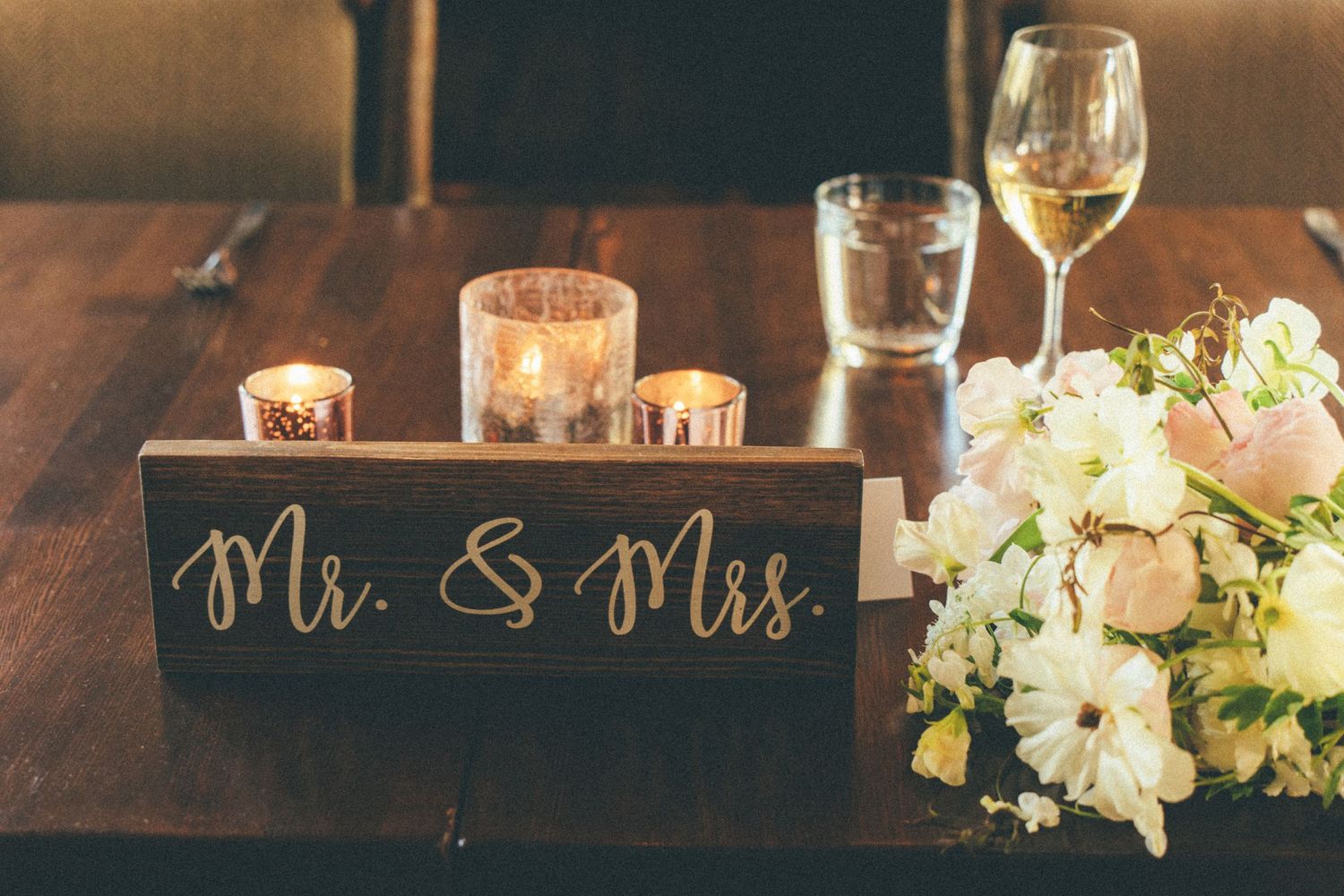 Mr. and Mrs. wooden sign with candles and white floral arrangement on rustic reception table.