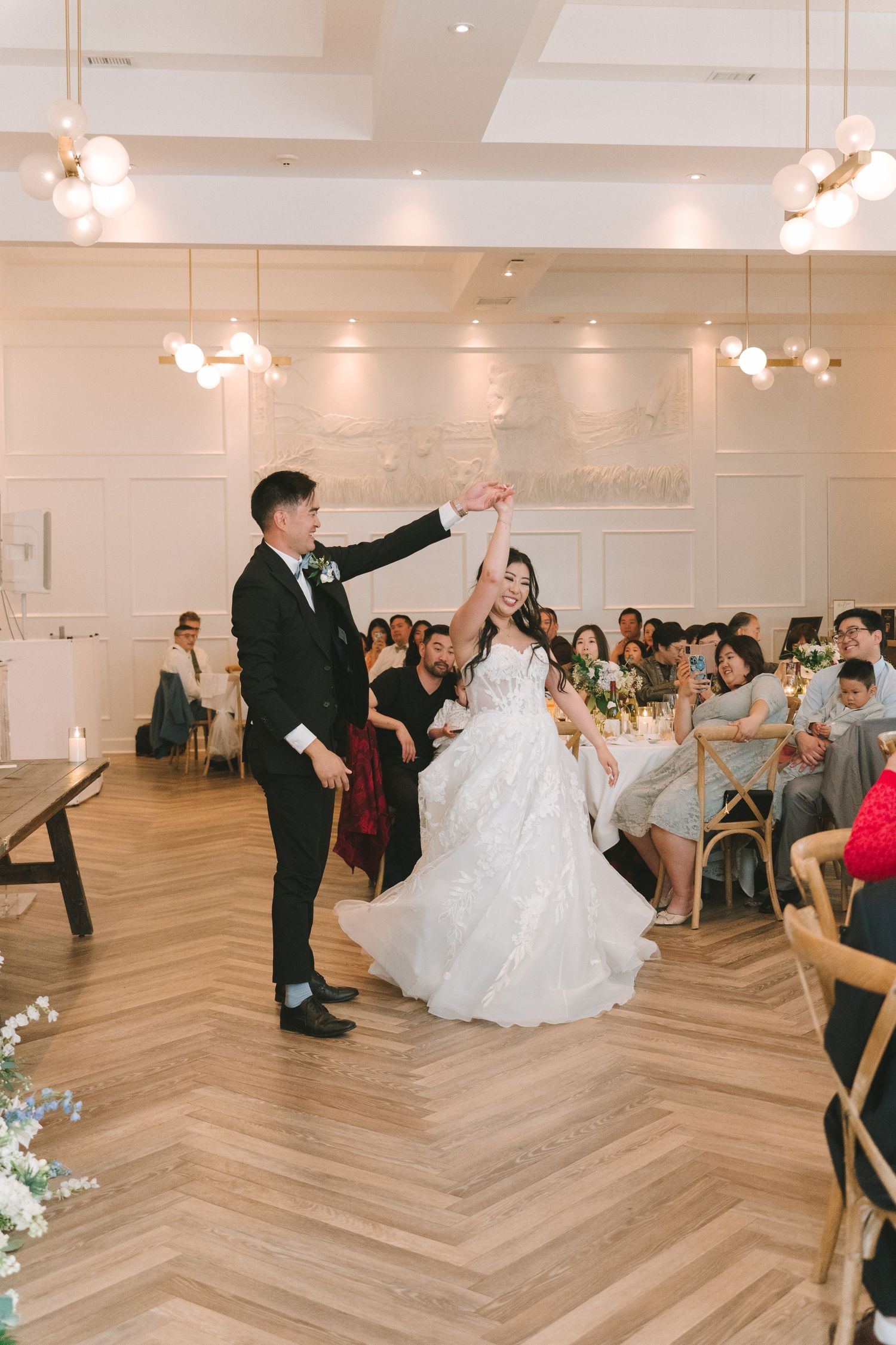 Bride and groom performing first dance spin in elegant white reception hall.