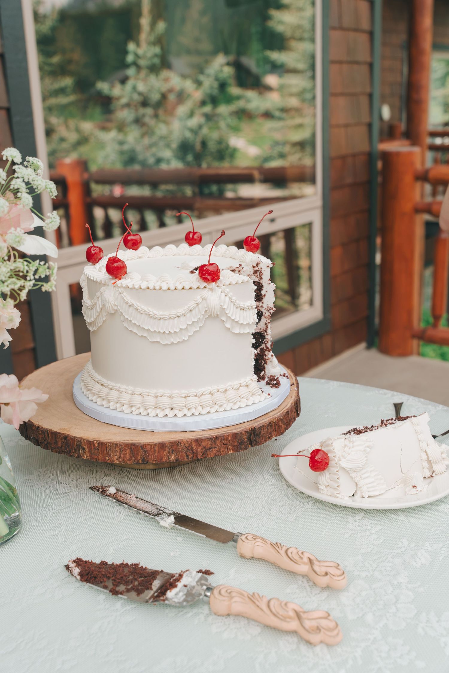 White wedding cake with cherries on wood slice stand, slice served.